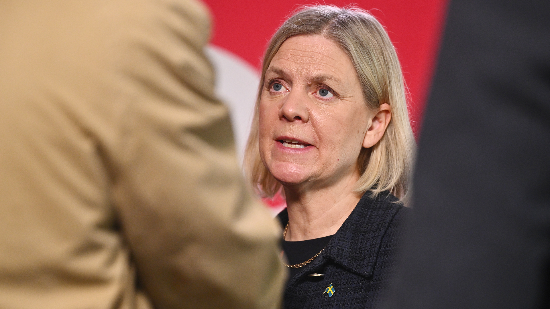 En kvinna med blont hår i samtal framför röd bakgrund