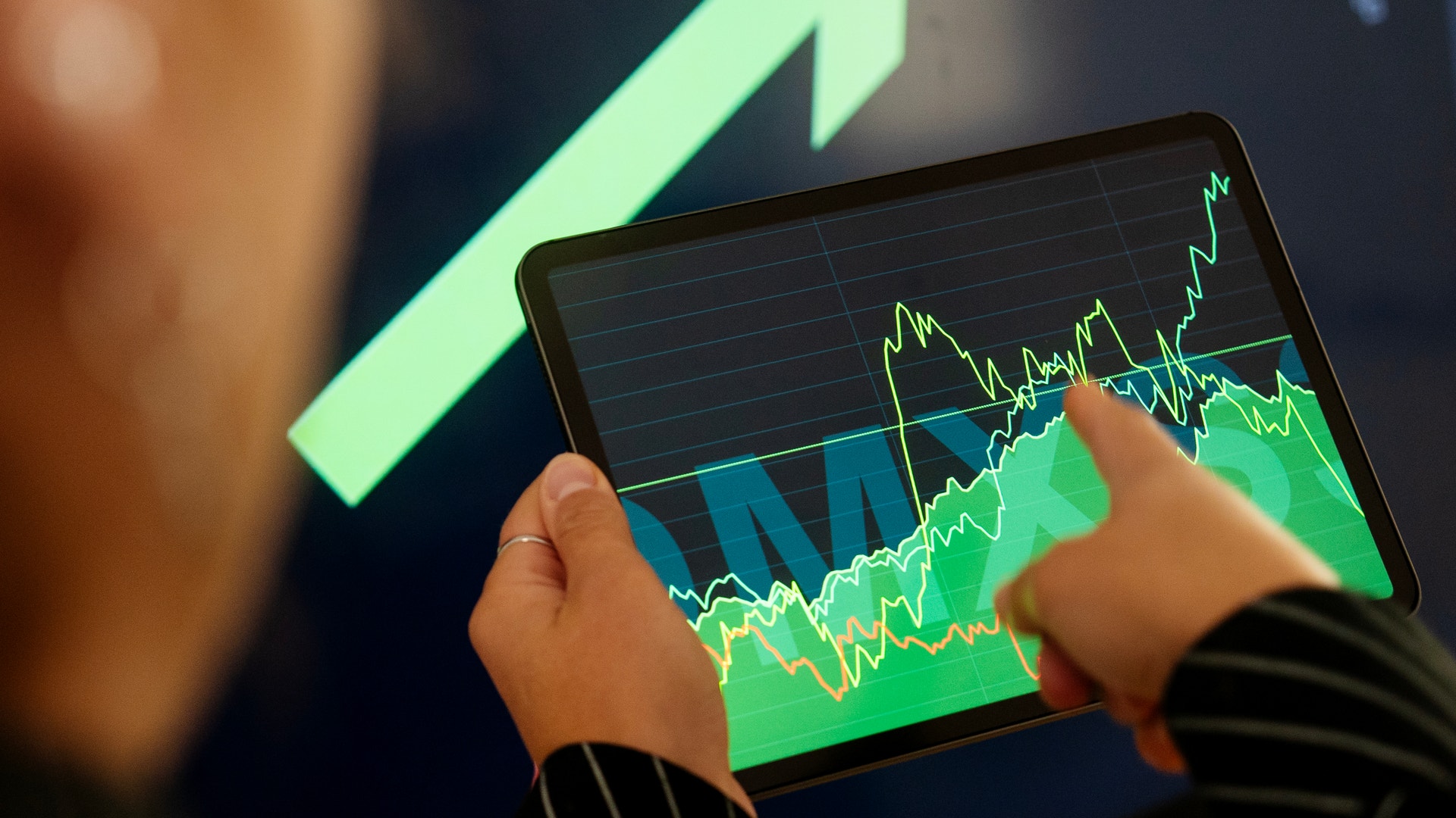 Person håller en tablet med gröna finansiella grafer och en stor uppåtpil som symboliserar ekonomisk tillväxt.