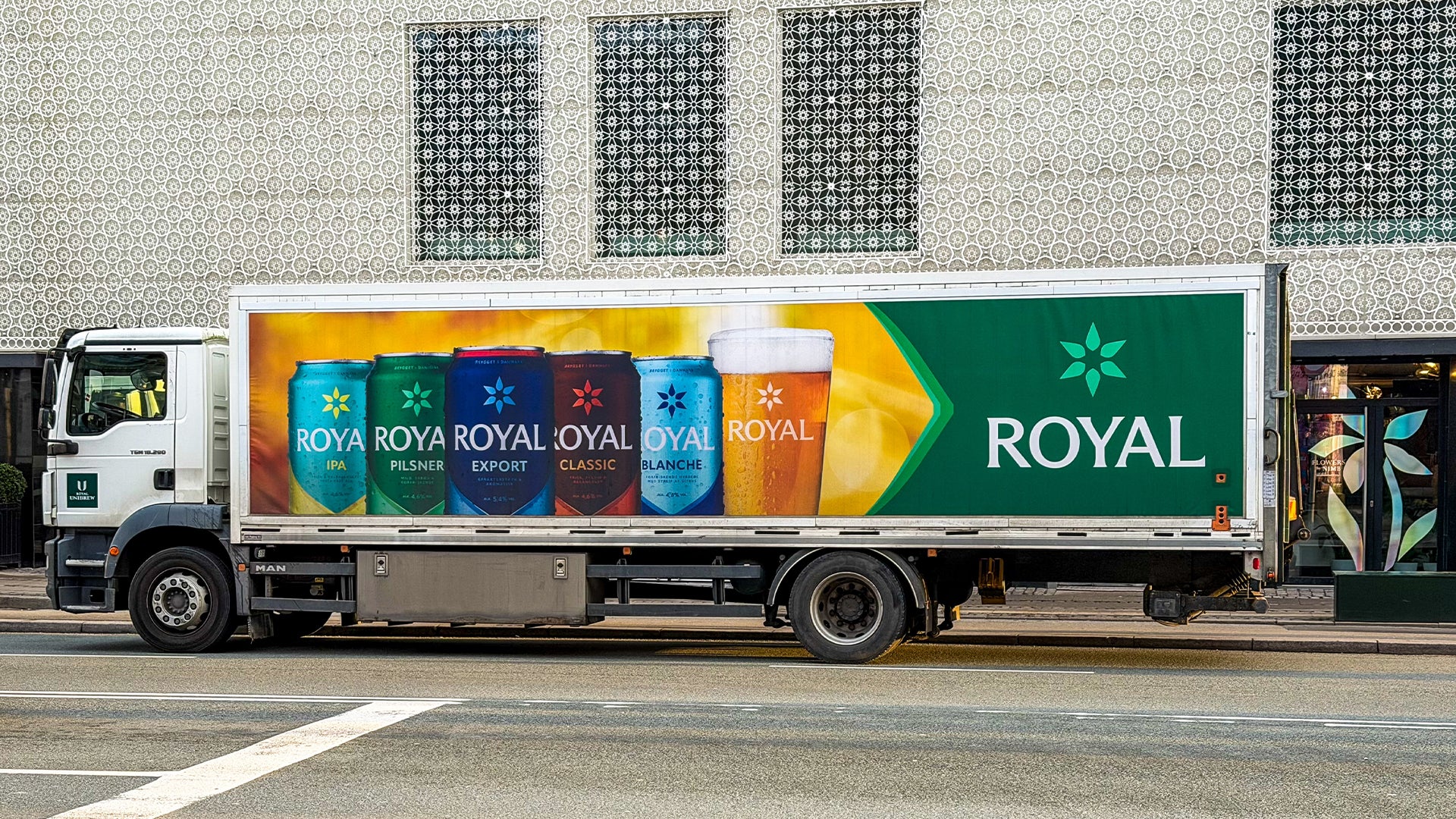 En lastbil med en stor färgglad reklambanner för Royal-märket, som visar olika färgade produkter och logotypen på sidan av fordonet.