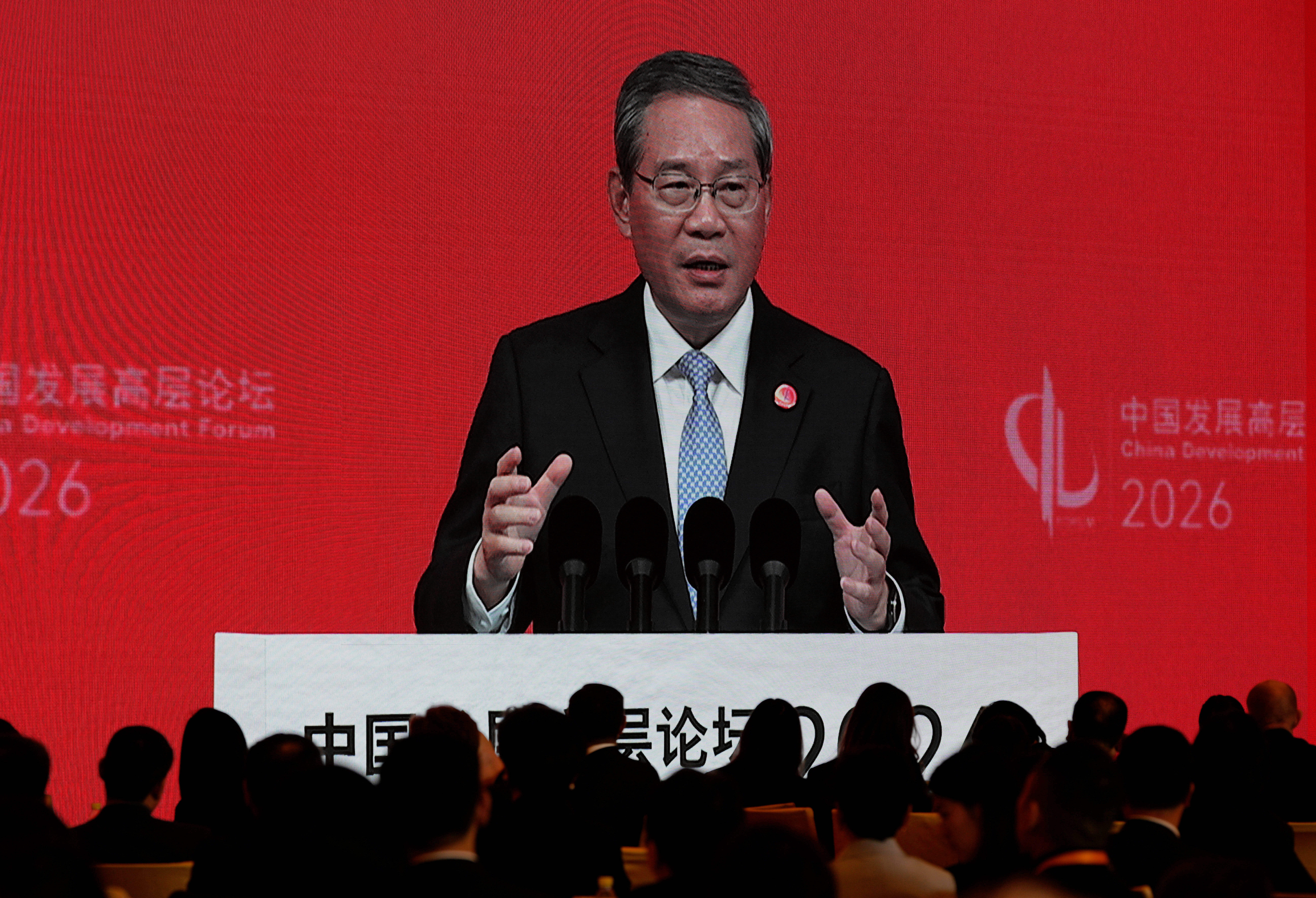 Premiärminister Li Qiang talar vid ett podium framför en röd bakgrund med publik