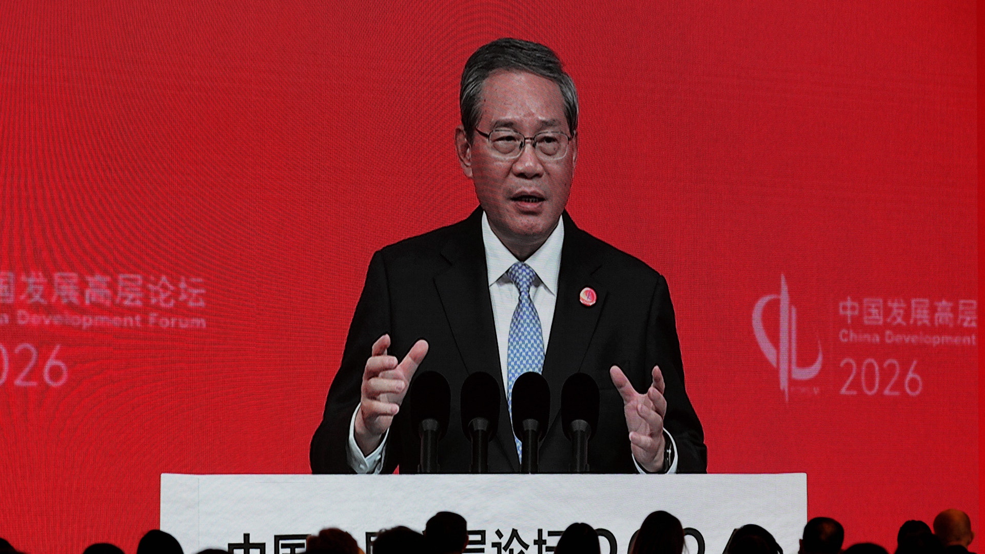 Premiärminister Li Qiang talar vid ett podium framför en röd bakgrund med publik