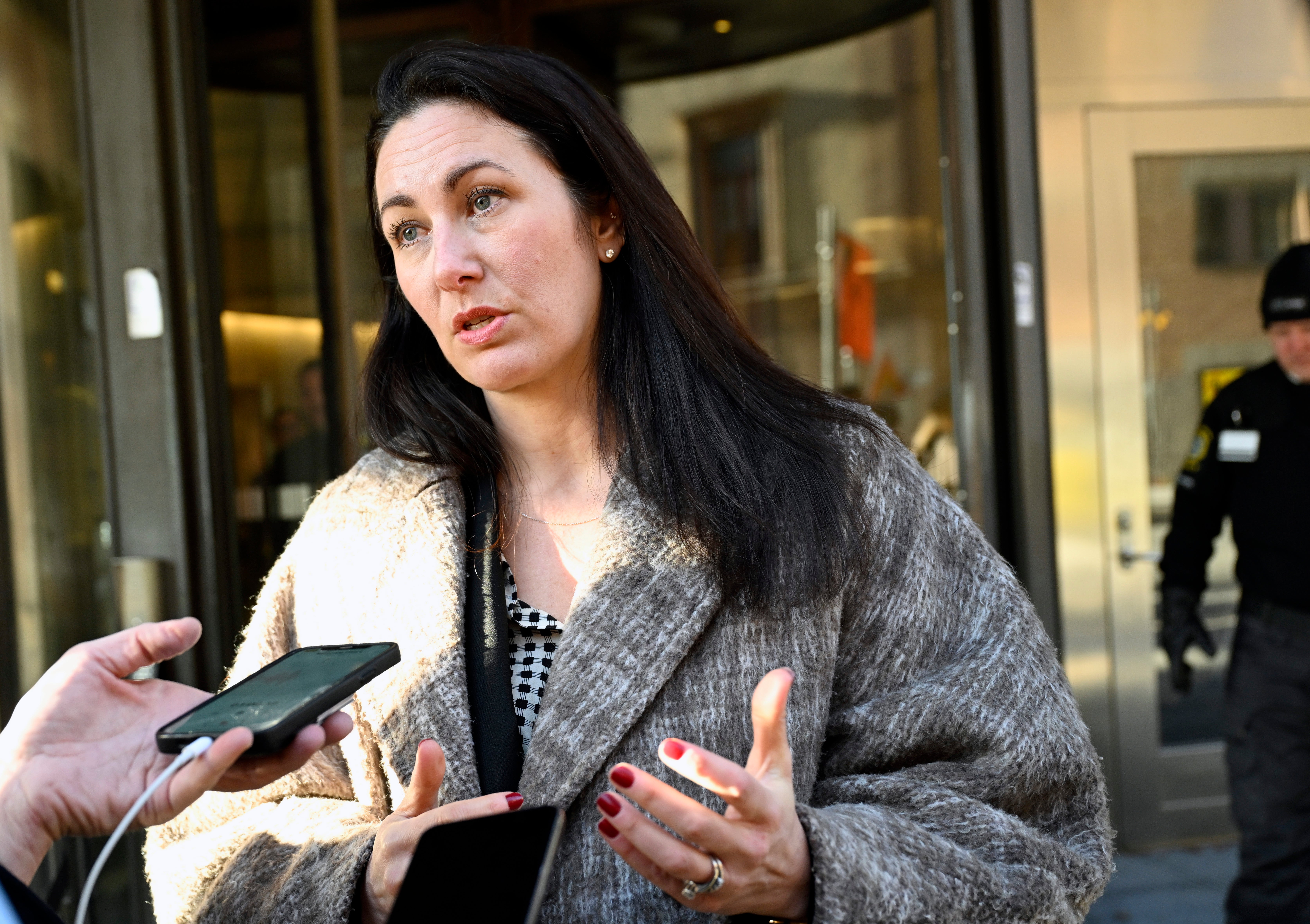 En kvinna intervjuas utomhus av journalister som håller fram mikrofoner mot henne.