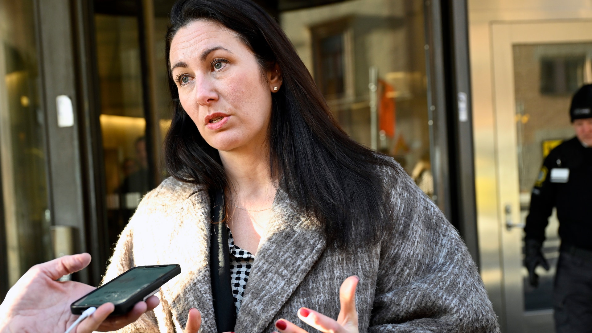 En kvinna intervjuas utomhus av journalister som håller fram mikrofoner mot henne.