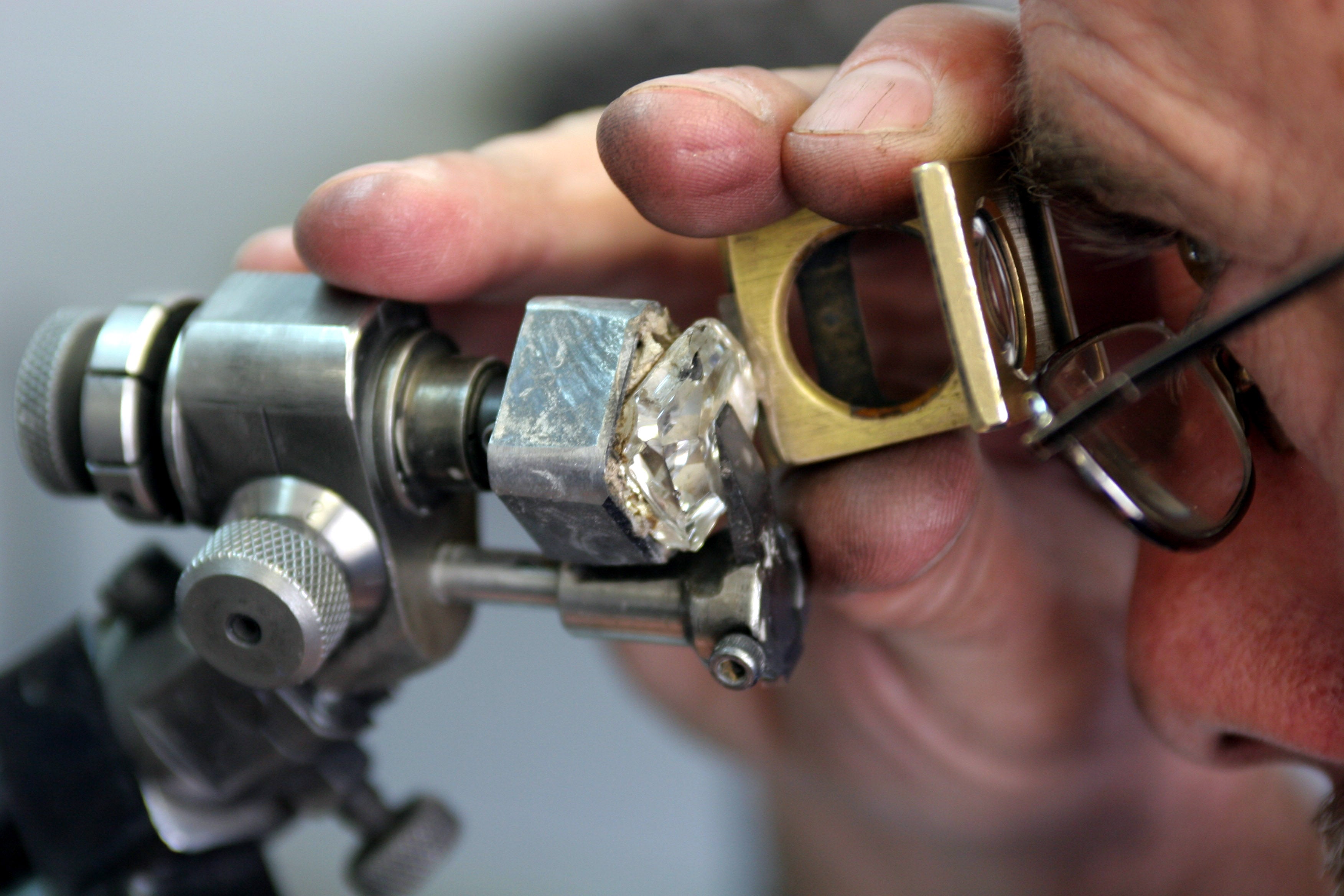 En man med glasögon granskar en oslipad diamant med ett förstoringsglas och ett mätinstrument.