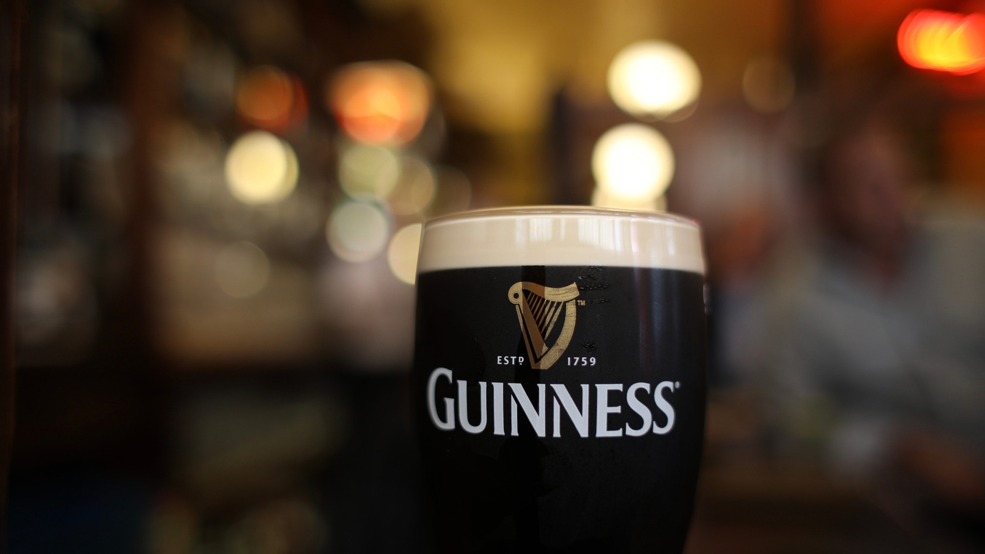 Ett glas Guinness öl med skummig topp på ett bord i en pub med suddig bakgrund av varmt ljus.
