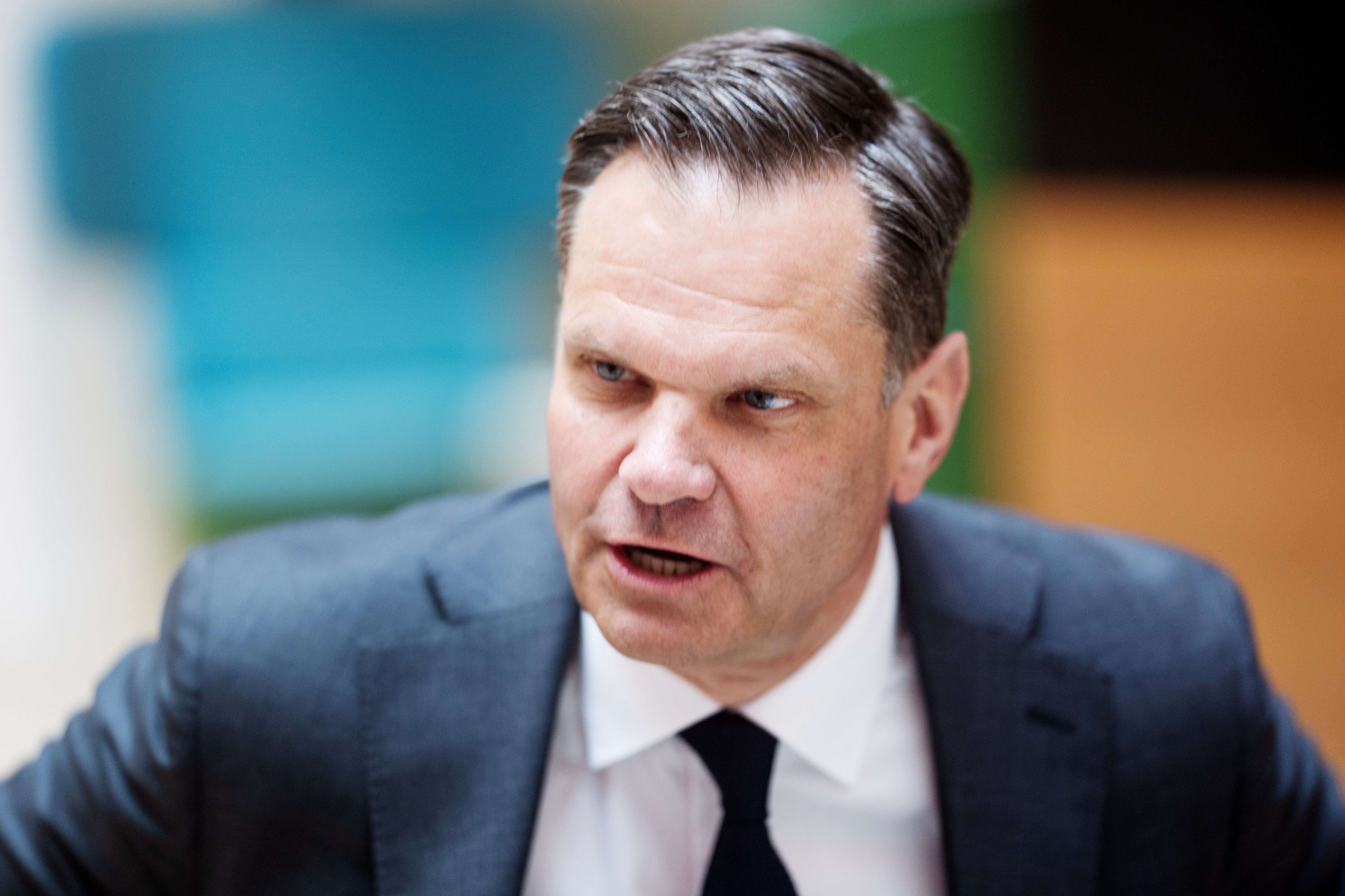 Porträtt av en man i mörkblå kostym och svart slips som talar eller presenterar något.