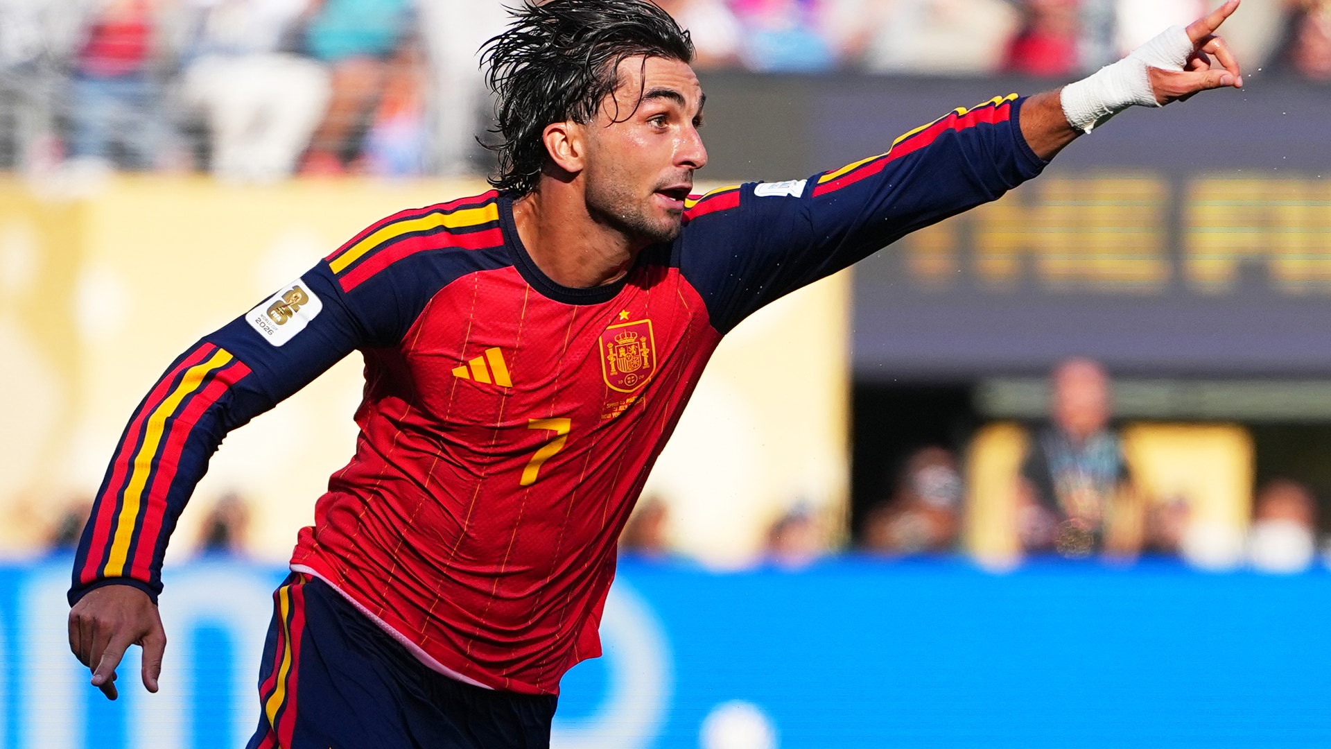 Fotbollsspelare i Spaniens röda landslagsdräkt gestikulerar under en fotbollsmatch med publik i bakgrunden.