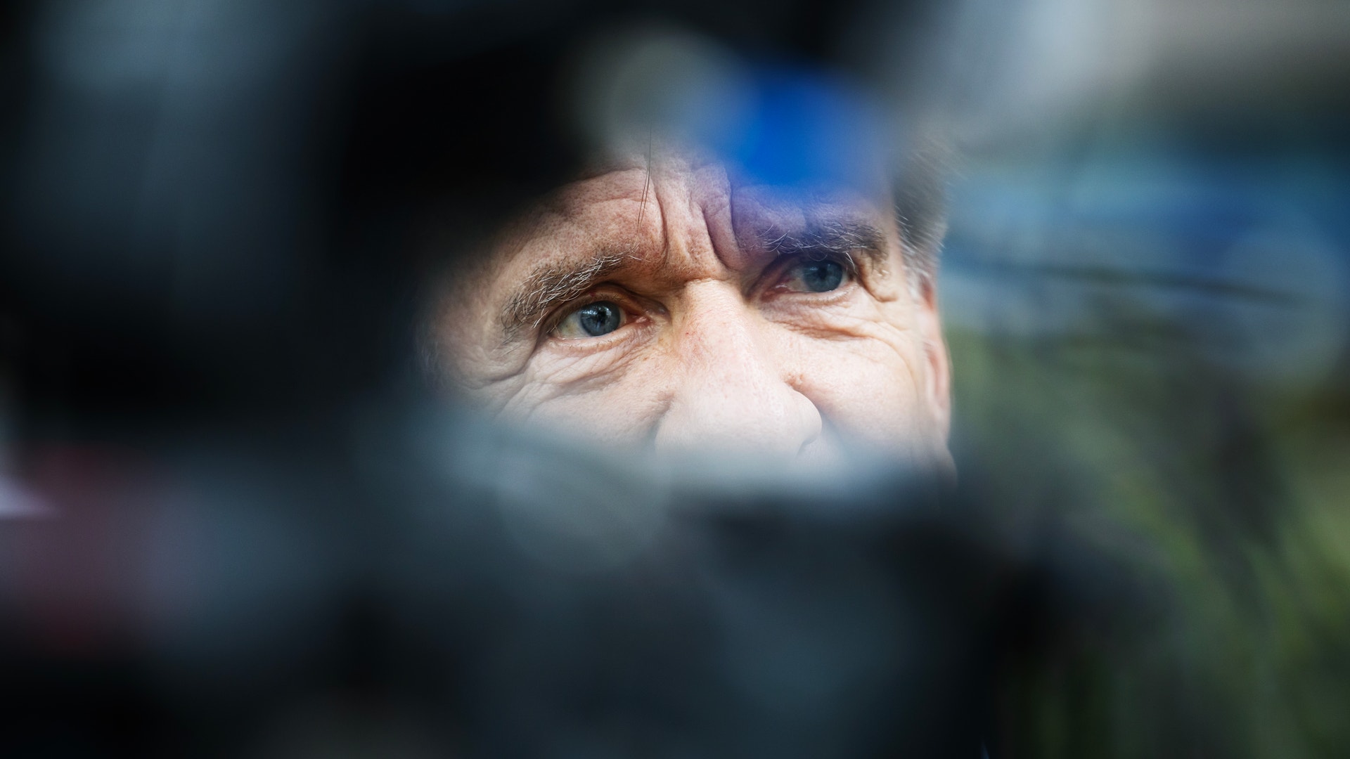 En man syns i närbild, fotograferad genom kamerautrustning som är oskarp i förgrunden.