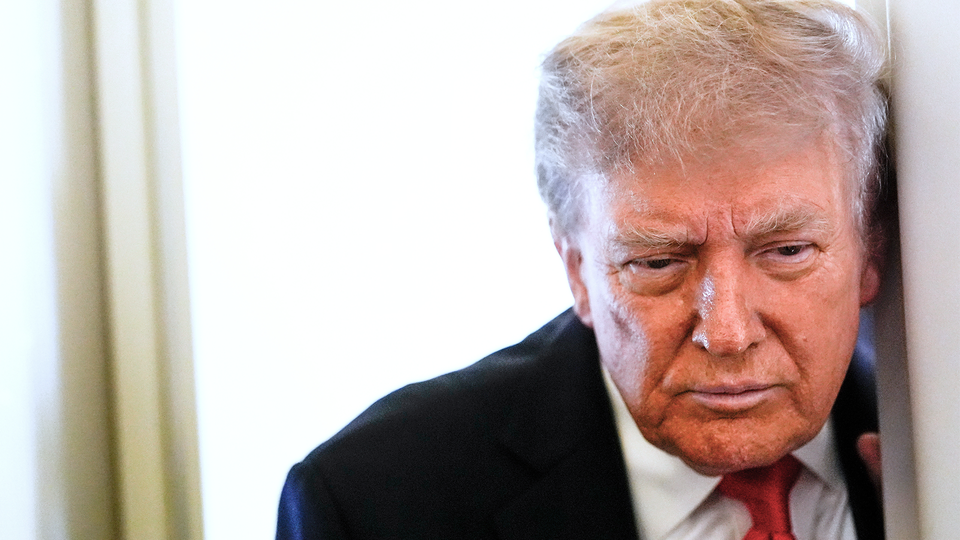 Donald Trump står och lutar sig mot en dörrkarm. Han tittar ner.