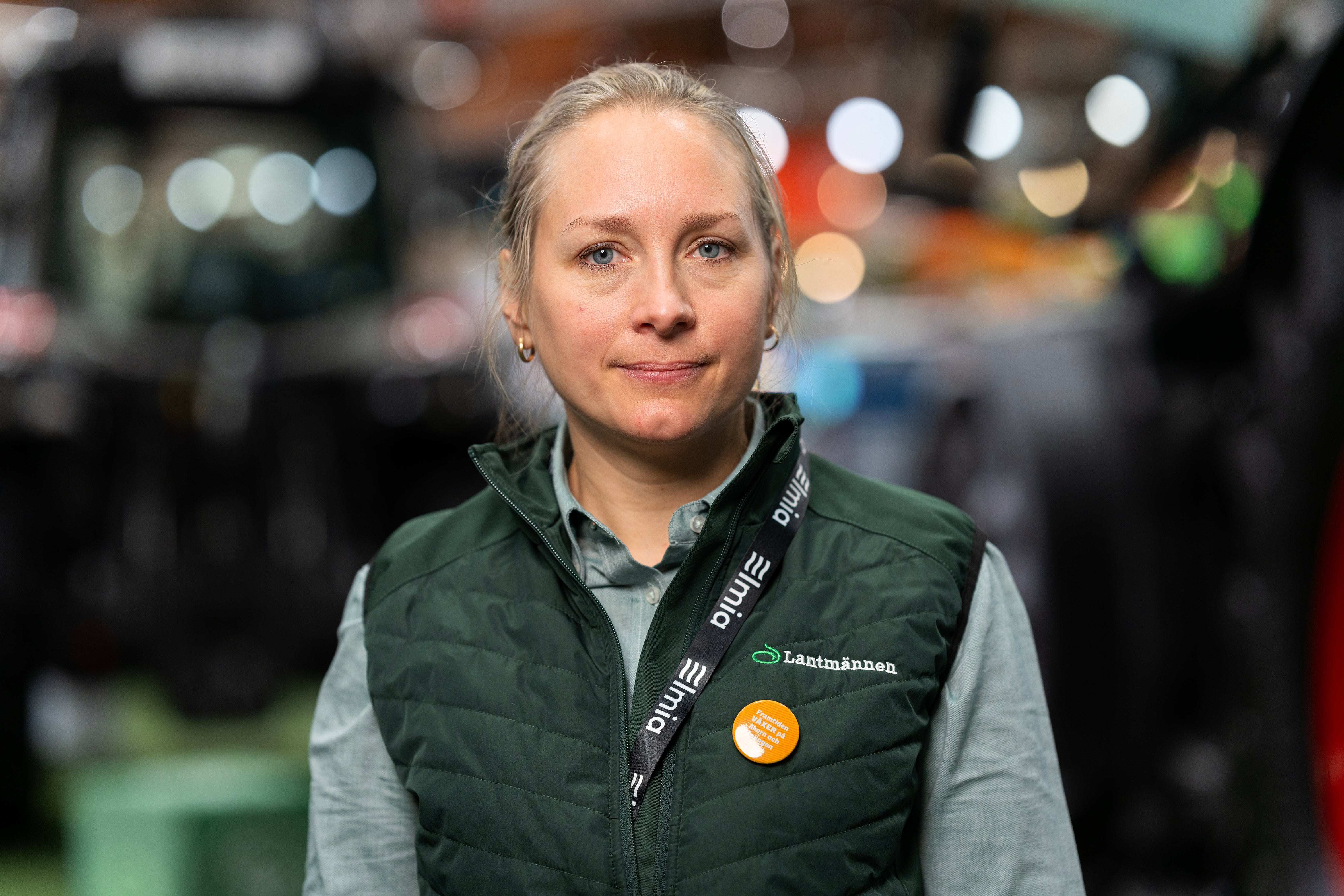 Porträtt av en leende kvinna med uppsatt hår i en grön väst med Lantmännens logotyp.