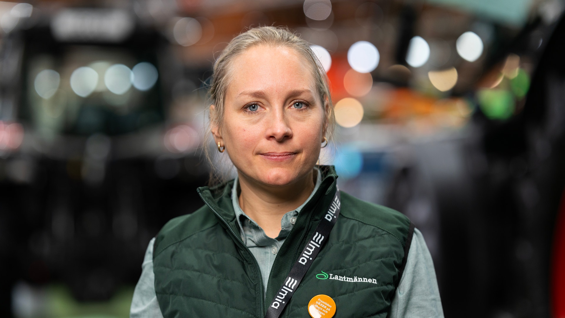Porträtt av en leende kvinna med uppsatt hår i en grön väst med Lantmännens logotyp.