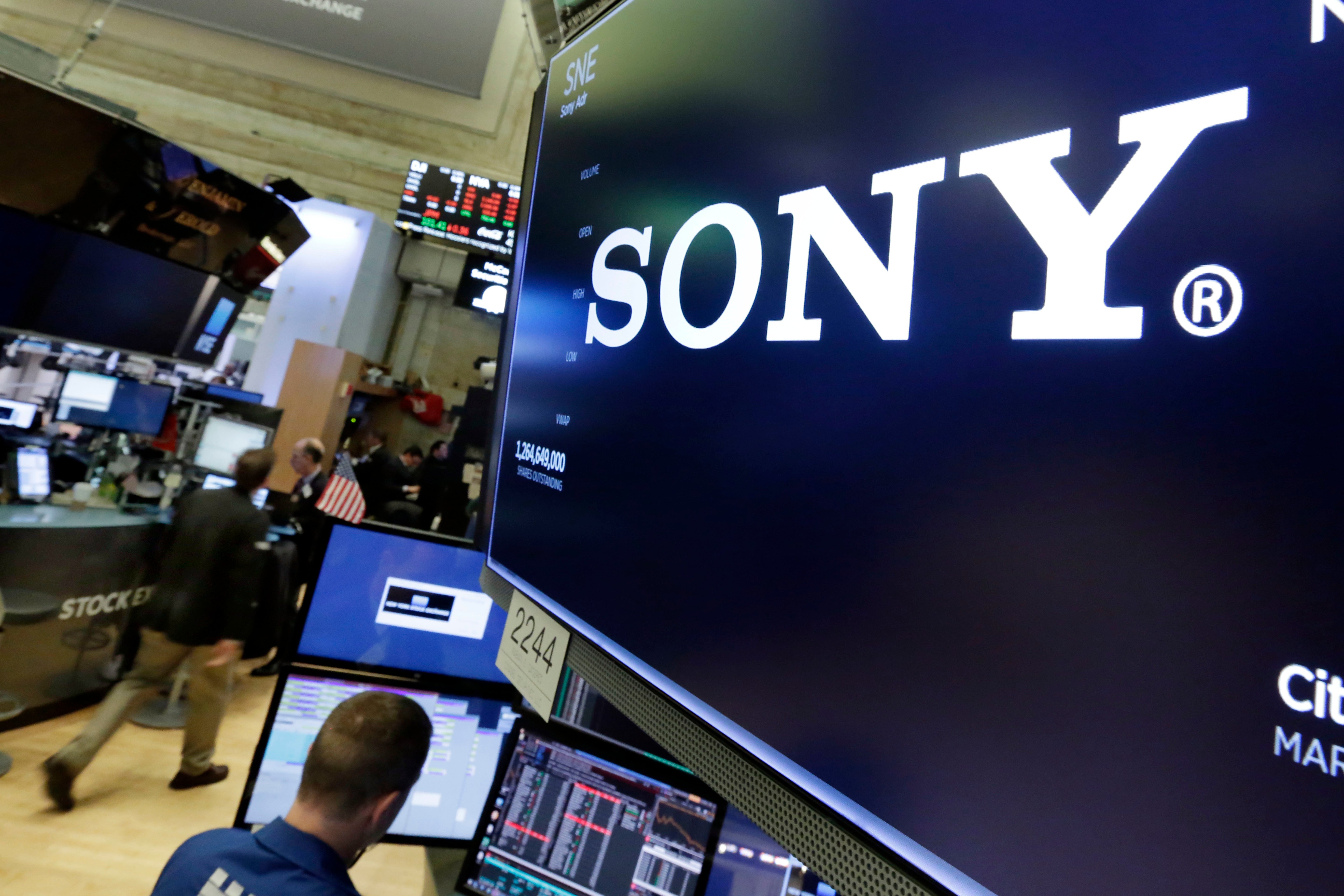 Sony-logotyp på en stor skärm på en handelsplats med arbetare och datorer i bakgrunden.
