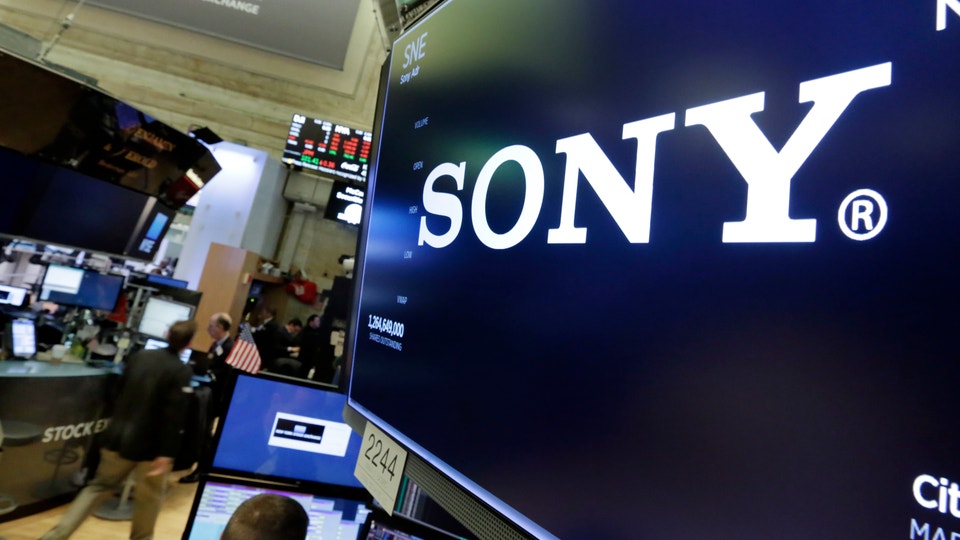 Sony-logotyp på en stor skärm på en handelsplats med arbetare och datorer i bakgrunden.