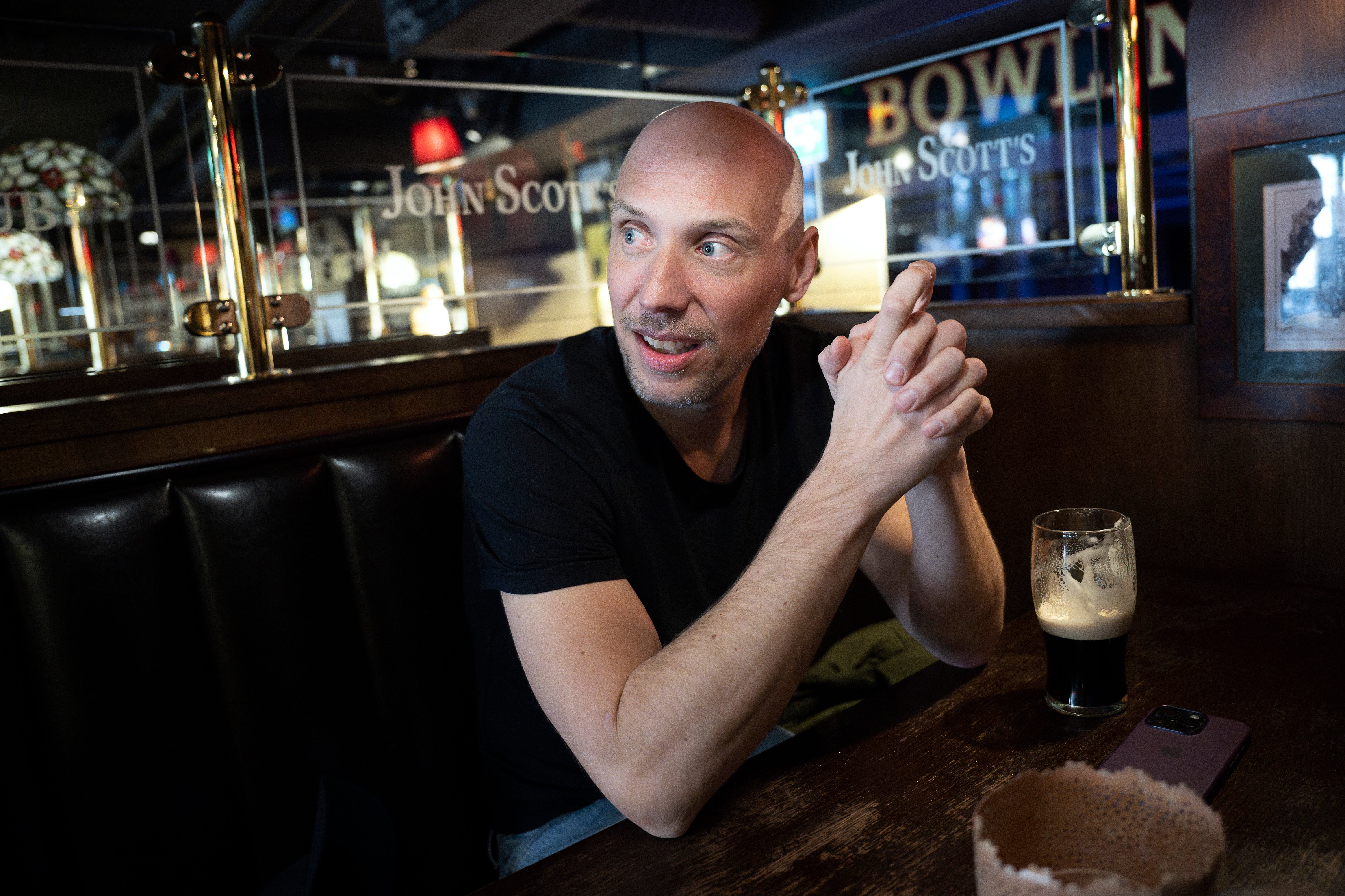 En man i svart skjorta sitter vid en bardisk med ett ölglas framför sig.