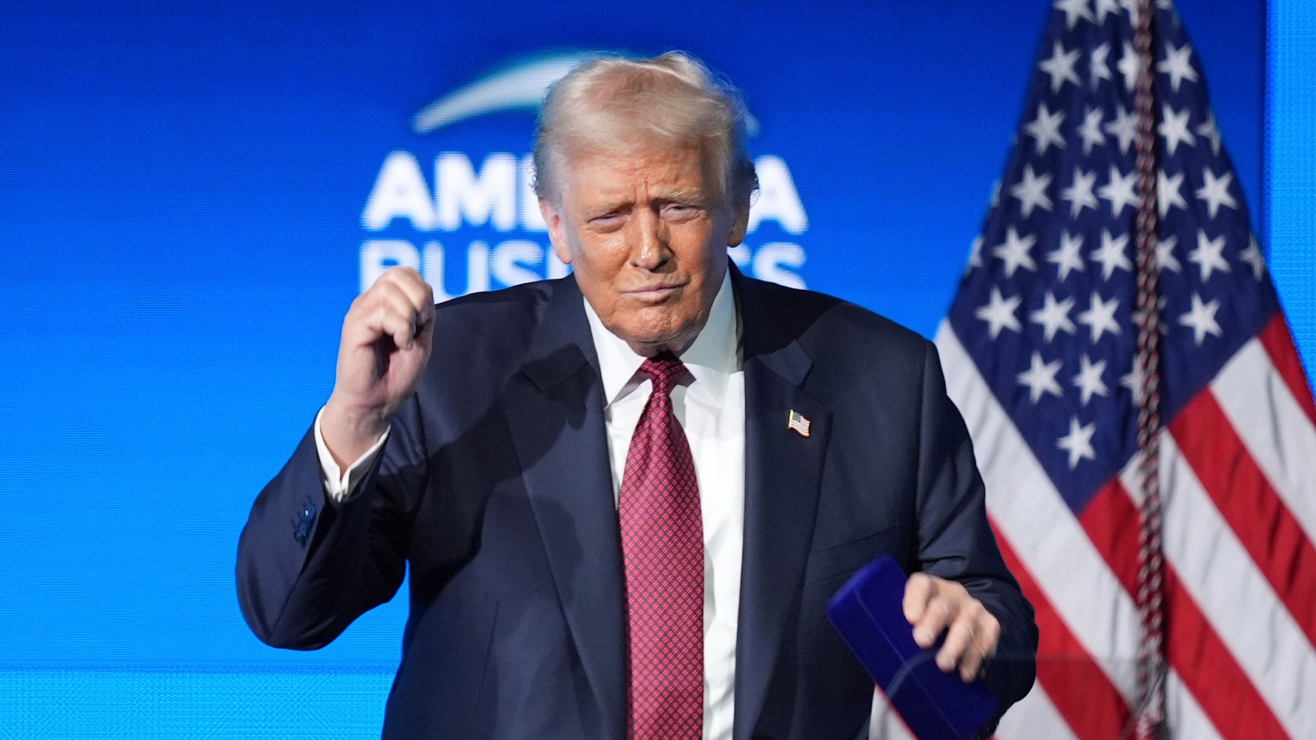 En man i kostym och slips står på en scen framför en amerikansk flagga.