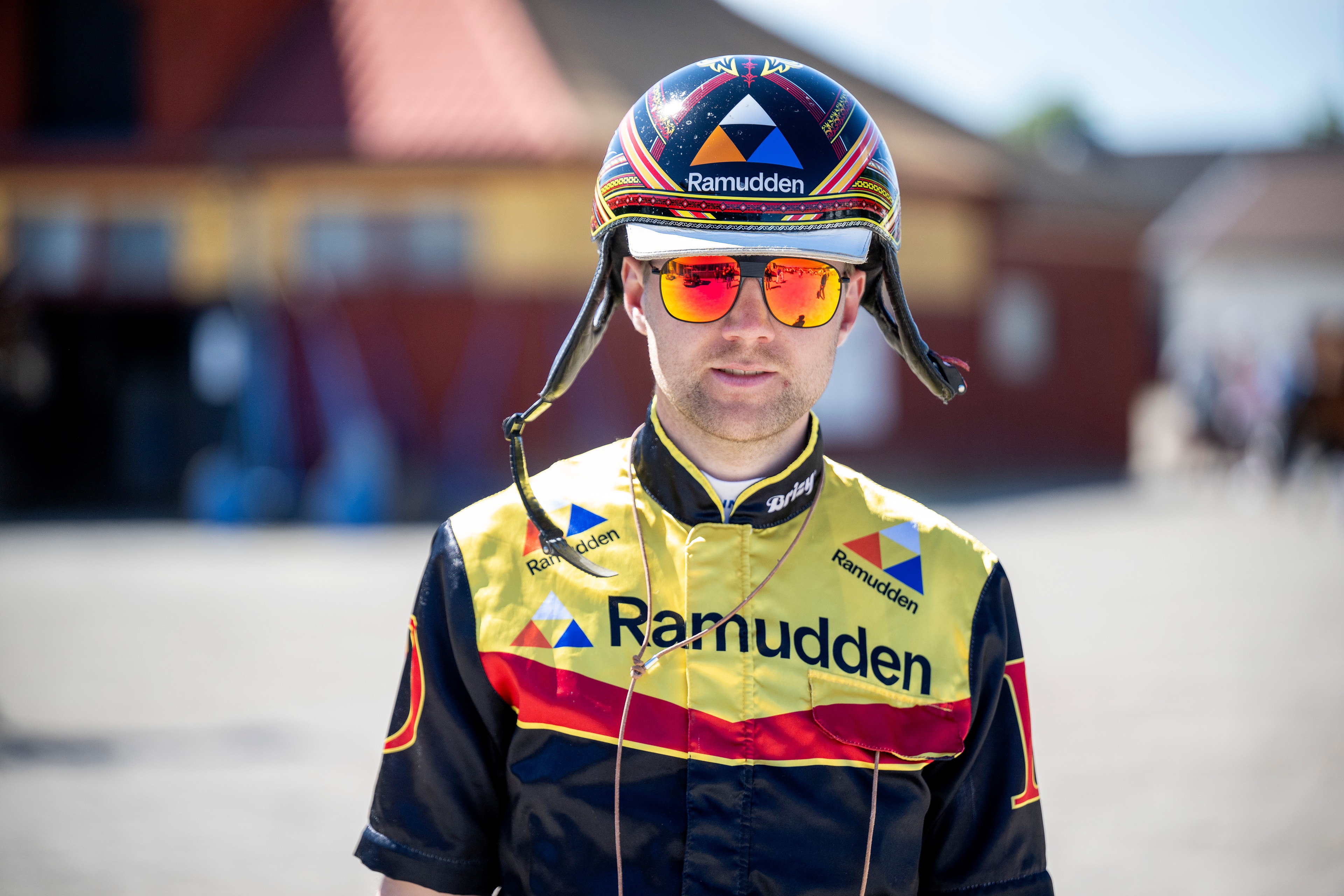 Porträtt av en person i gul och svart sportdräkt med Ramudden-logotyp, röda solglasögon och mössa. Personens ansikte är vänt direkt mot kameran.