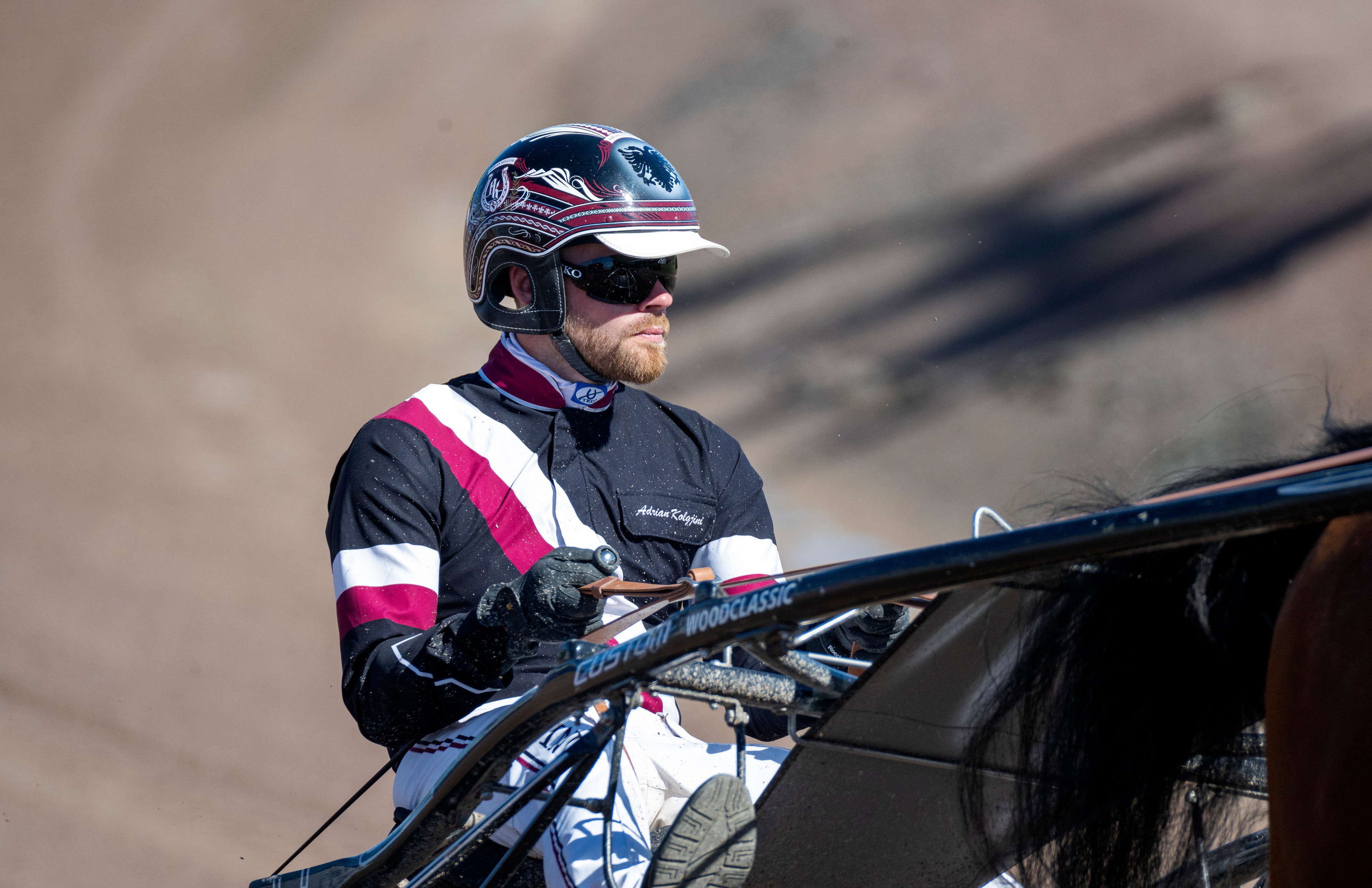 En jockey i racing-utrustning med hjälm och färgglada kläder står bredvid en travväg på Solvalla.
