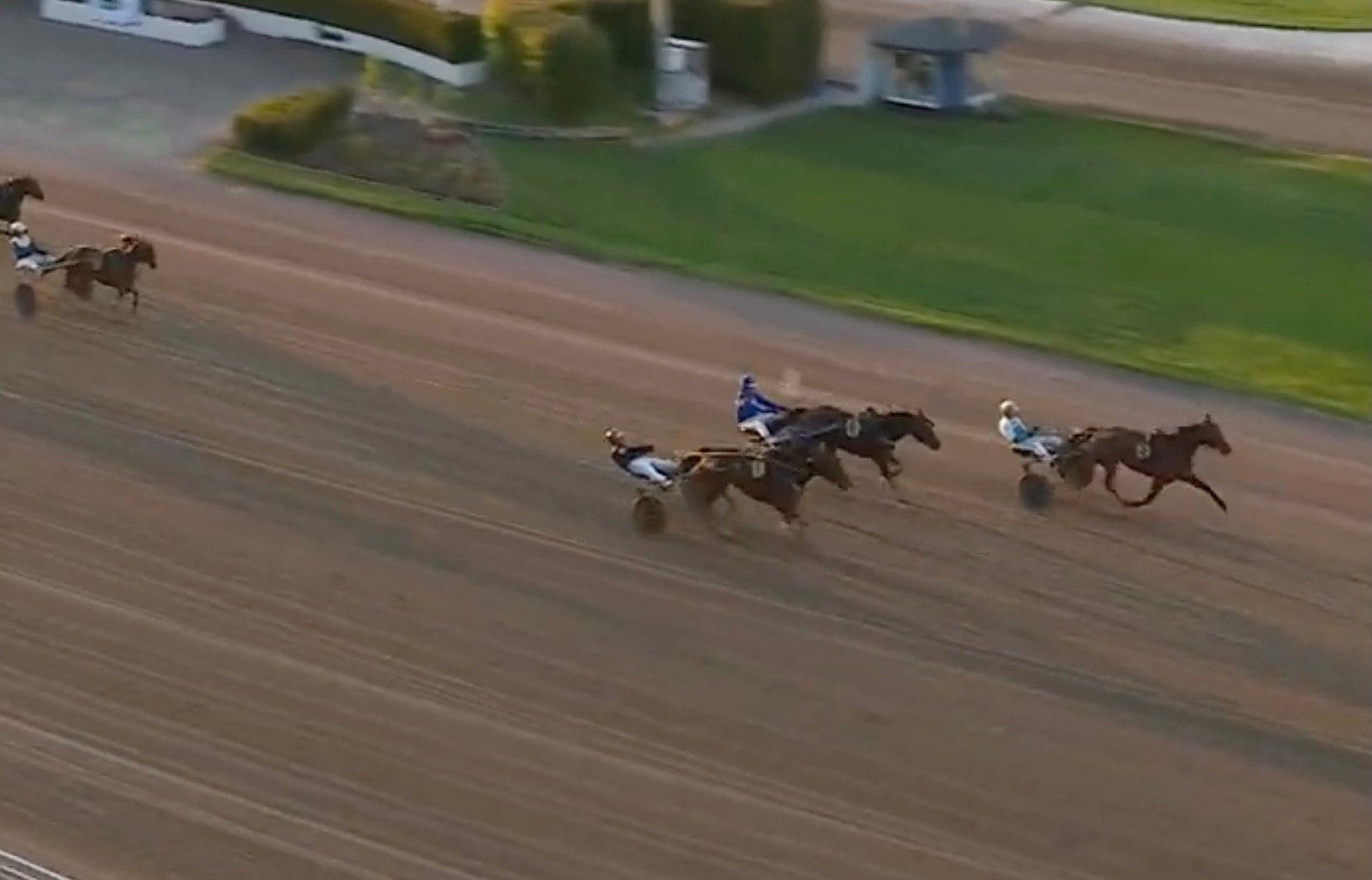 Travlopp med flera hästar och kuskar som tävlar på en sandtrack. Hästarna drar vagnar med kuskar i blå och vita färger.