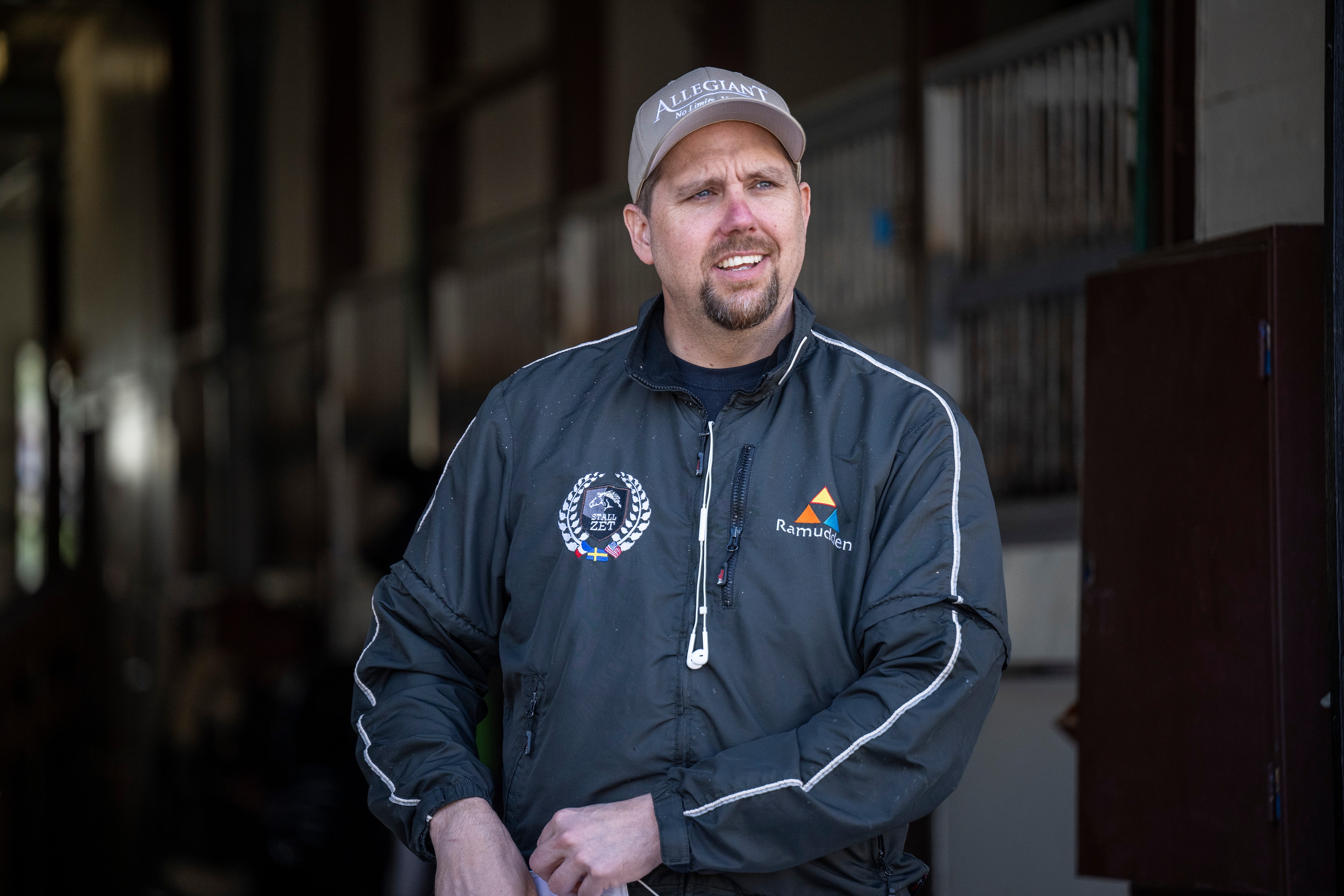 Porträttfoto av en man i mörkblå jacka och vit keps som står inomhus.