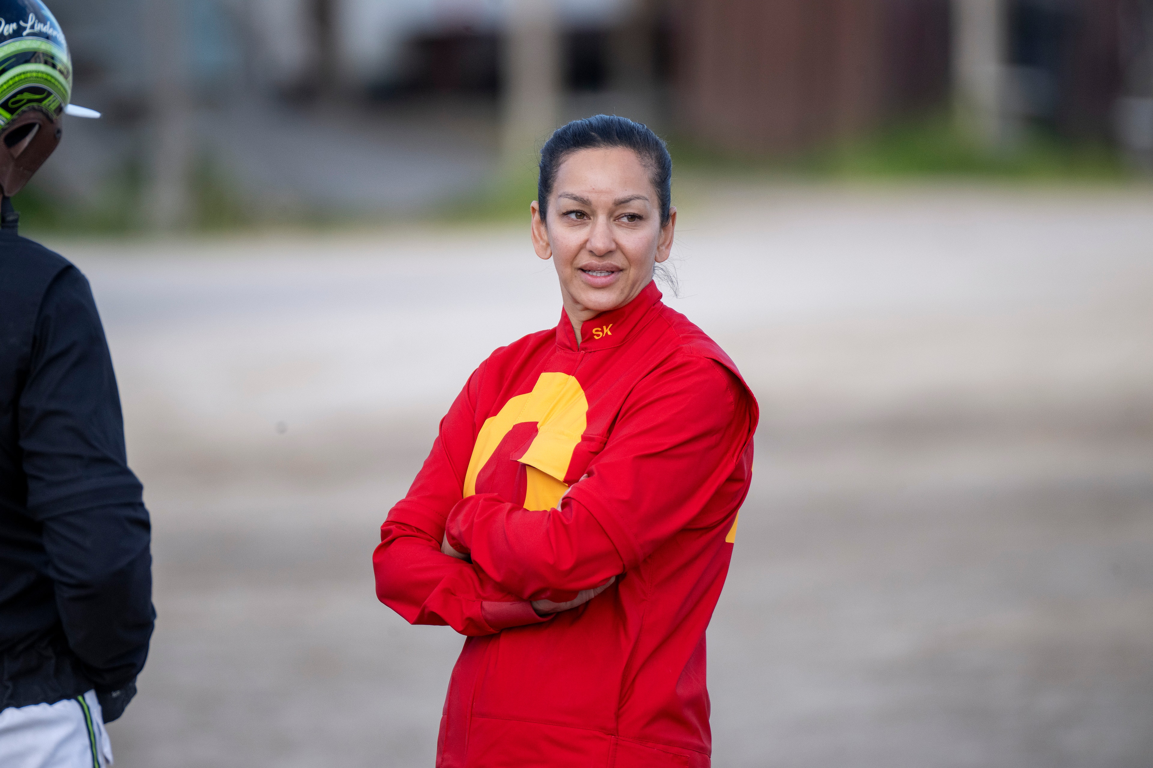 Porträtt av en kvinna i röd träningsjacka som står utomhus på en sportplats.