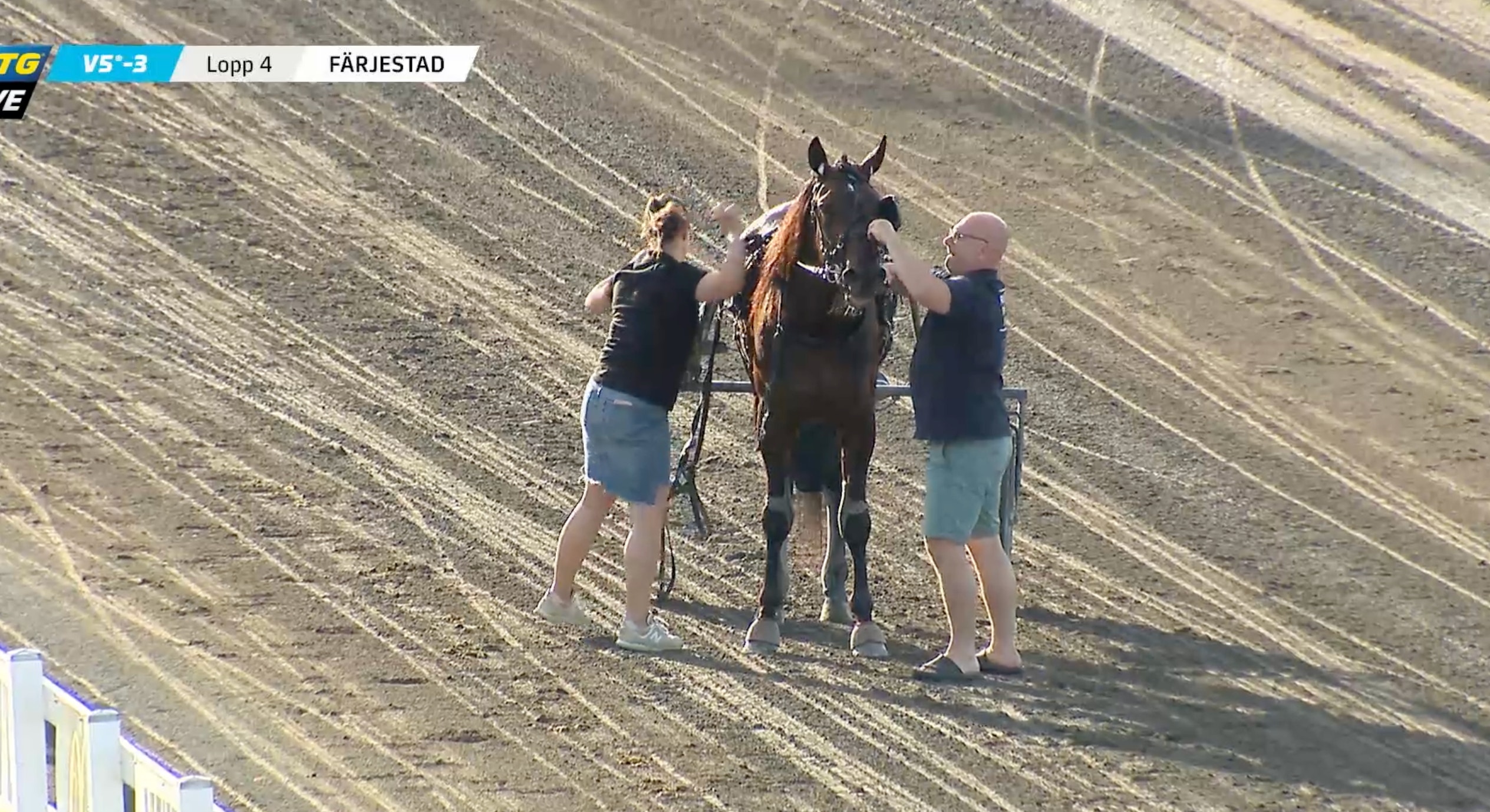 Två personer står med en häst på en sandbanor vid ett hästelopp.