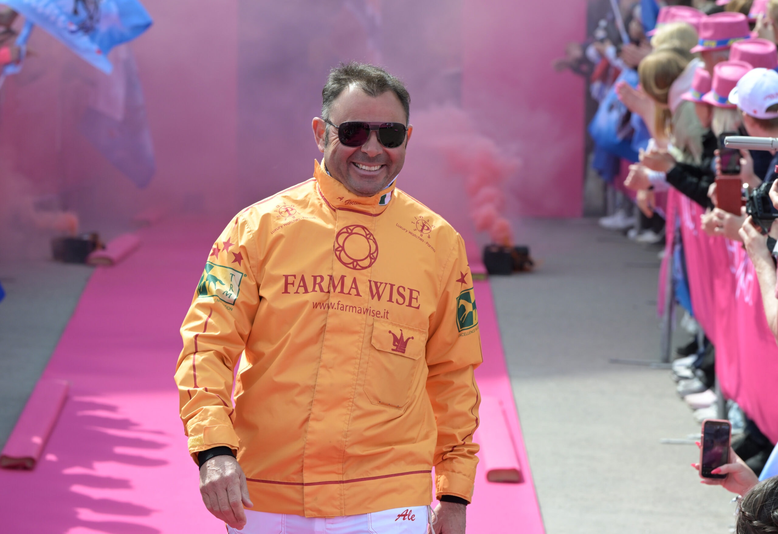 Man i orange racingoverall går på rosa bana under invigningscermoni med publik på sidorna.