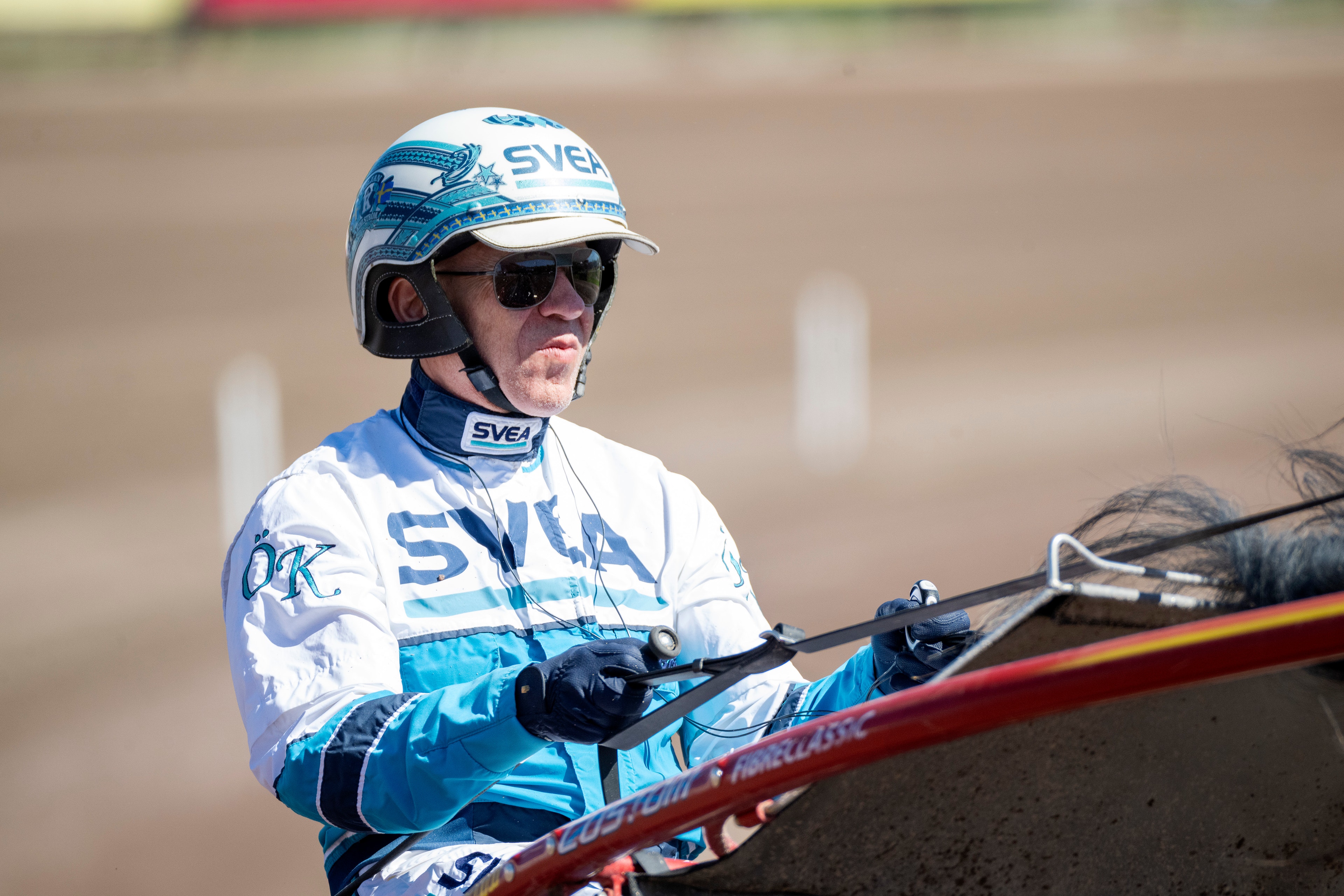 En speedway-förare i blå och vit skyddsutrustning sitter på en speedway-motorcykel på en tävlingsbana.
