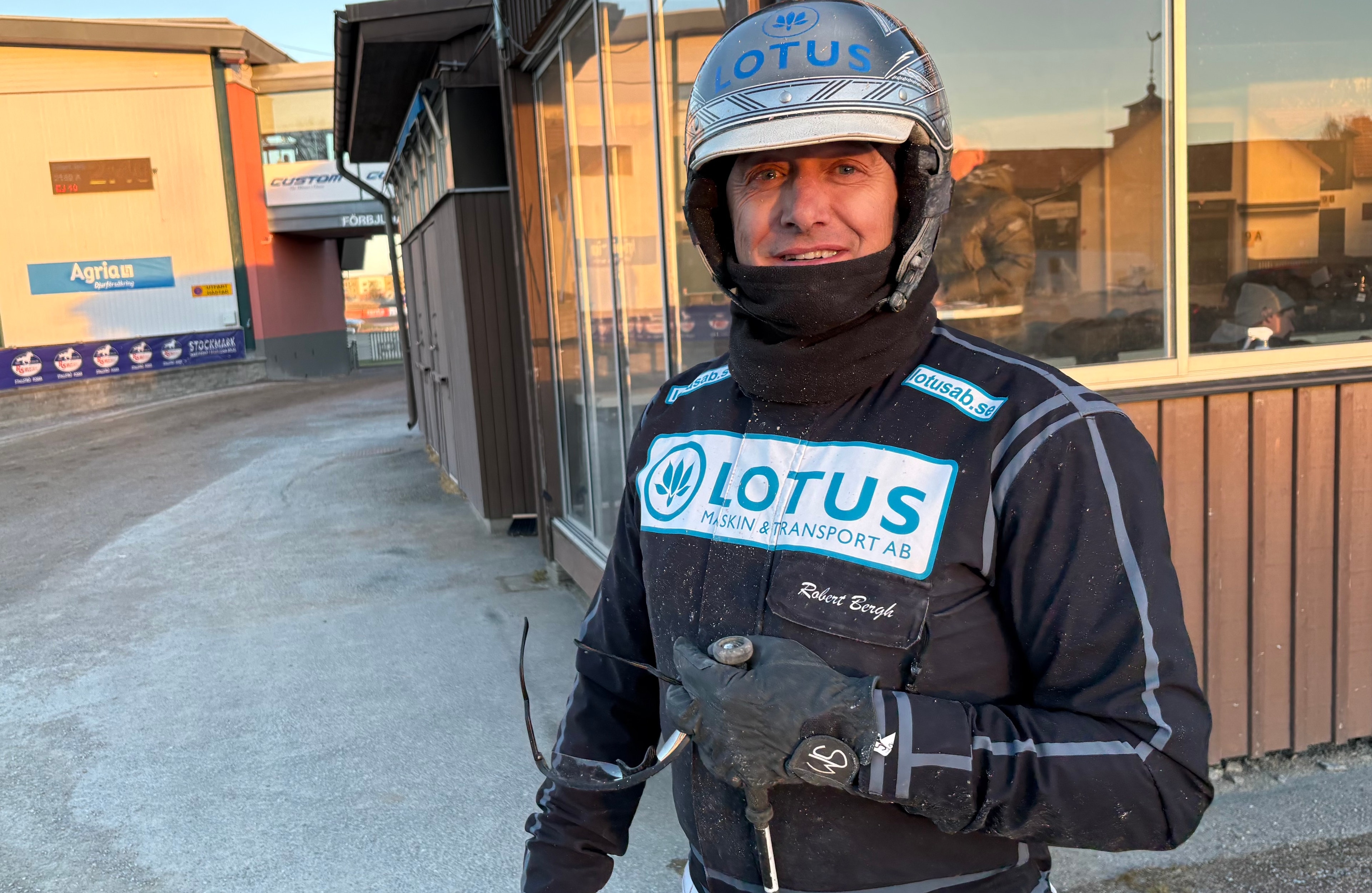 Porträttfoto av en man i svart racing-outfit med Lotus-märkning och motorsport-hjälm.