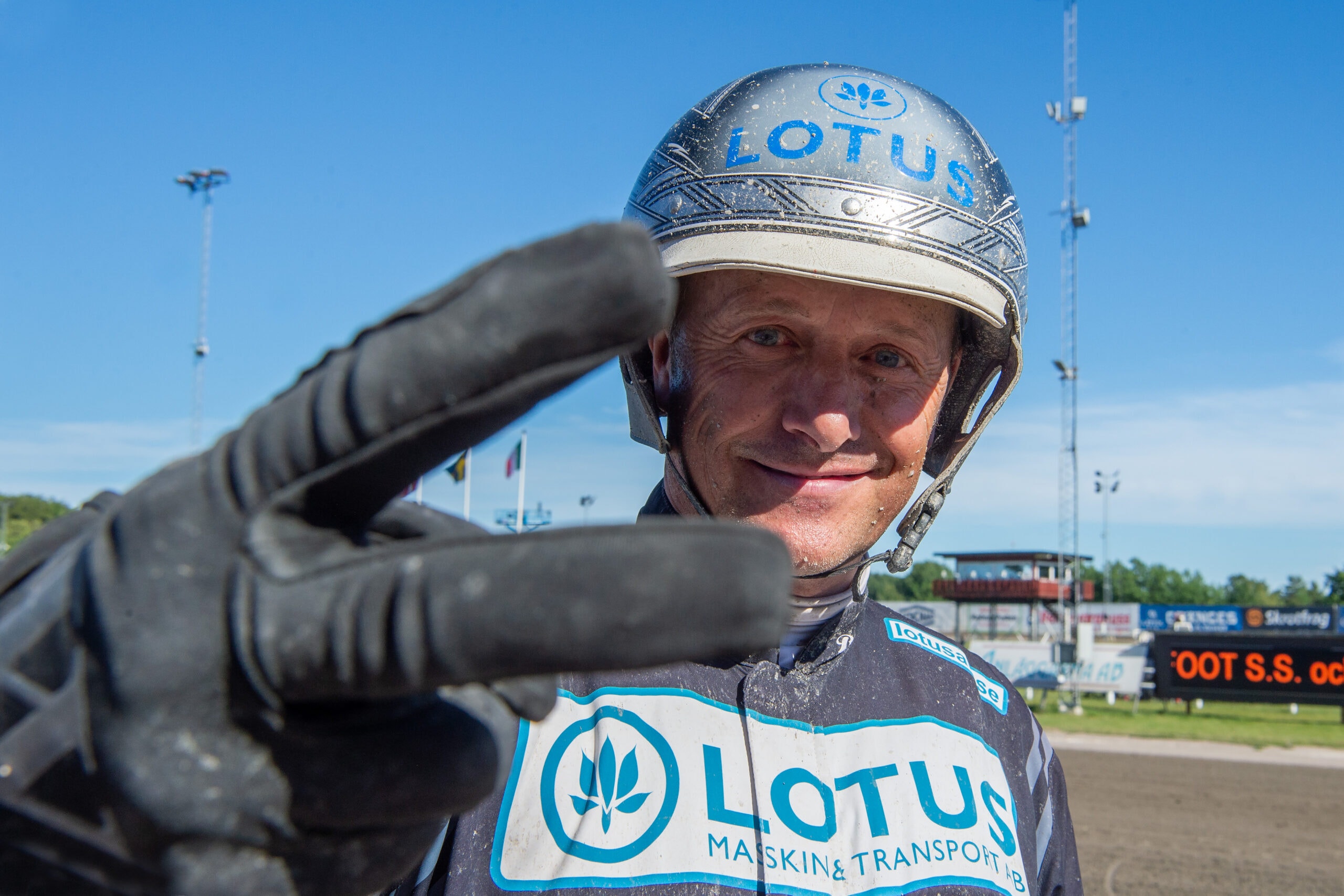 Porträttbild av en speedway-förare i racing suit och hjälm märkt Lotus, som poserar vid en speedway-bana.