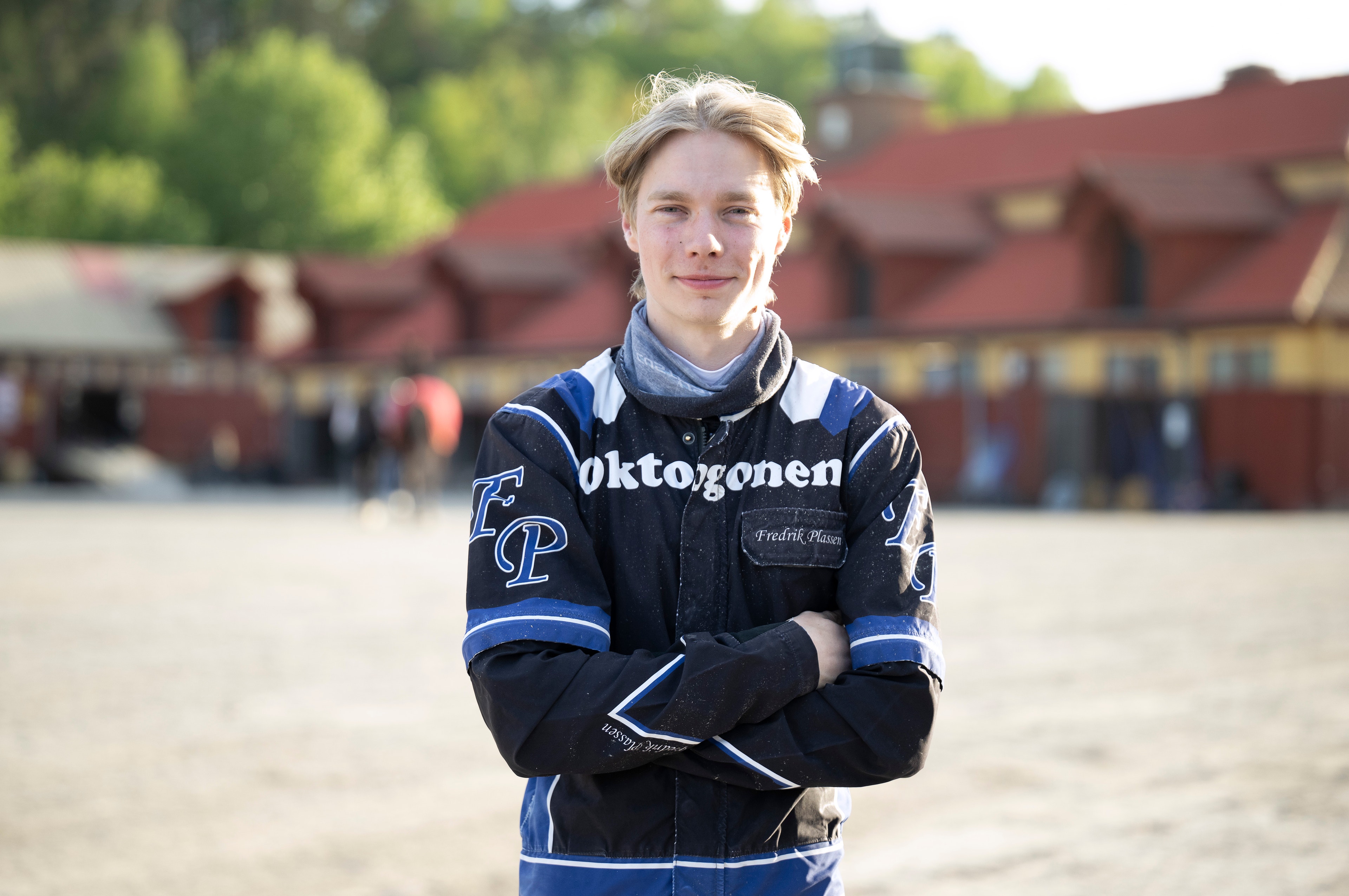 Porträtt av en ung person som står framför en ridanläggning. Personen bär en mörkblå jacka och ser in i kameran.