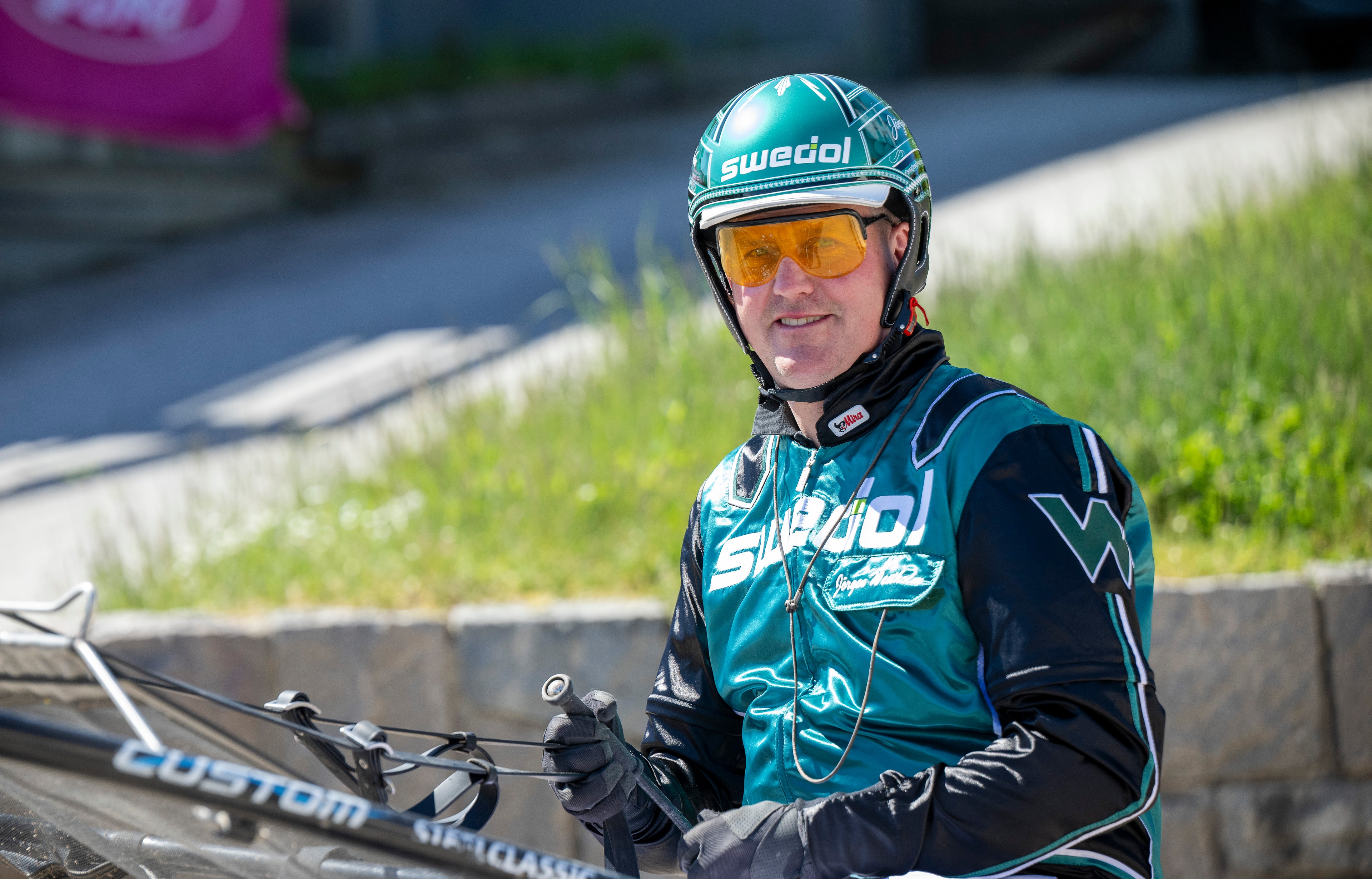 En cyklist i teal- och svartfärgad cykelkläder och vit cykelhjälm med gula solglasögon sitter på en cykel och poserar för kameran.