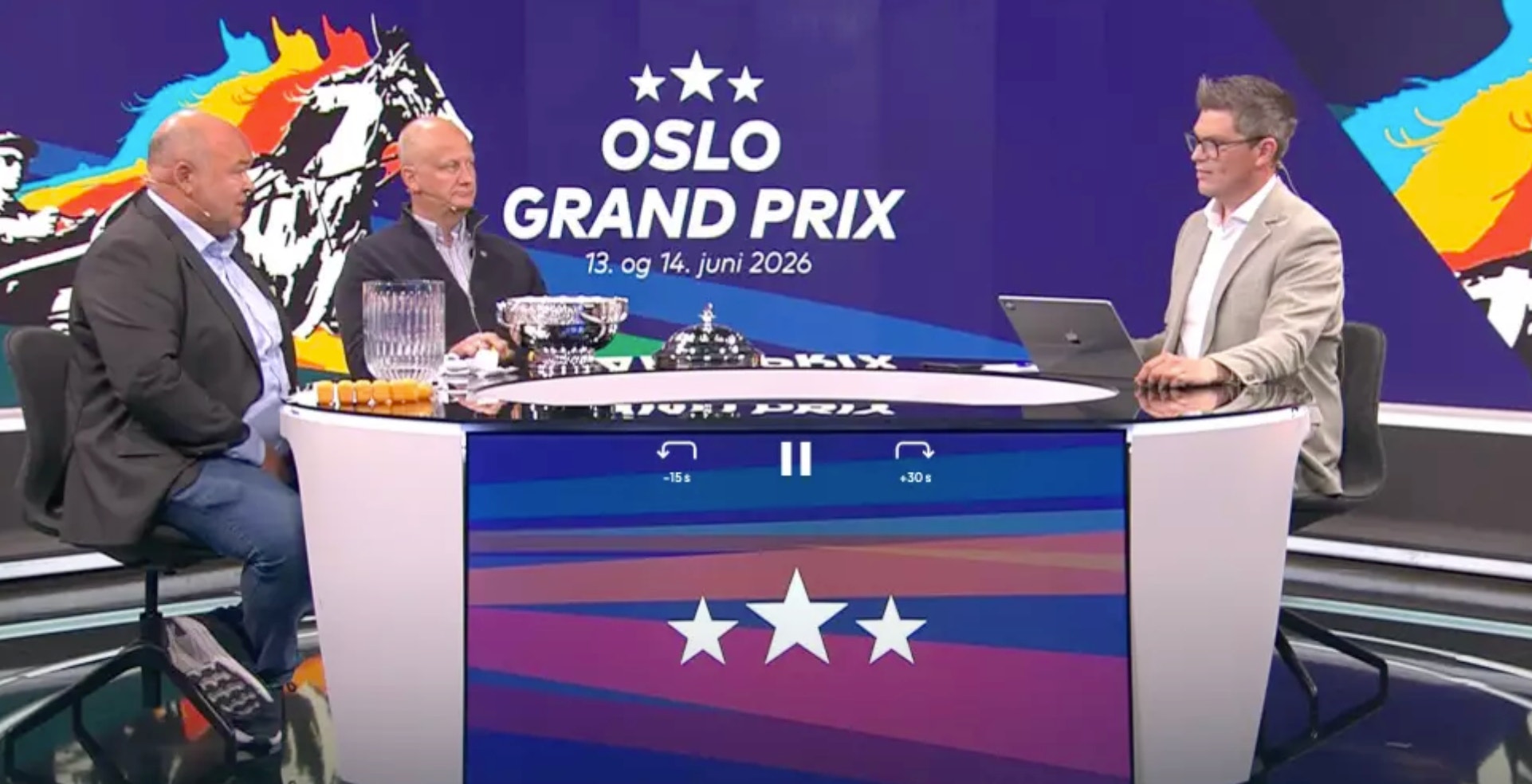 Två män sitter vid ett studiobord under en TV-sändning om Oslo Grand Prix motorsportevent. I bakgrunden syns logon och färgglad grafik för evenemanget.