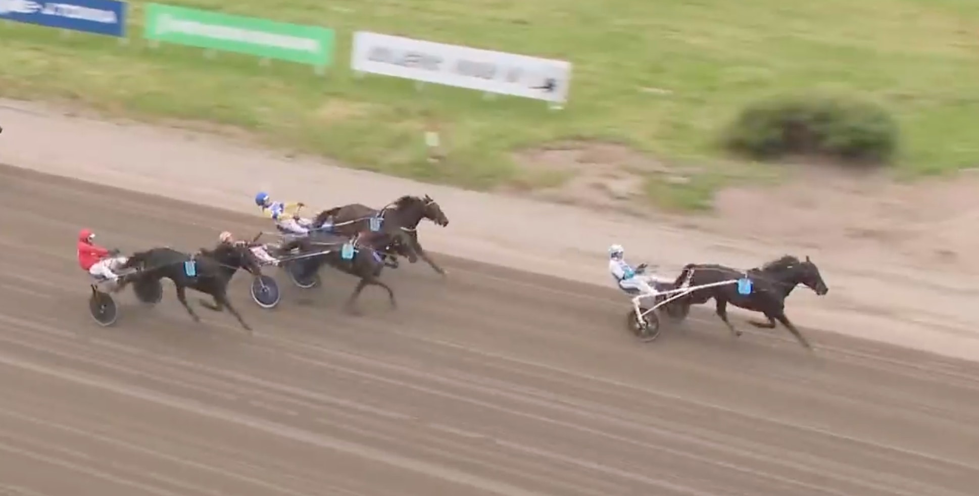 Hästkapplöpning på en sandtrack med två hästar som dras av kuskar i sulkyvagnar. En häst med röd kusk på vänster sida och en häst med vit kusk på höger sida.