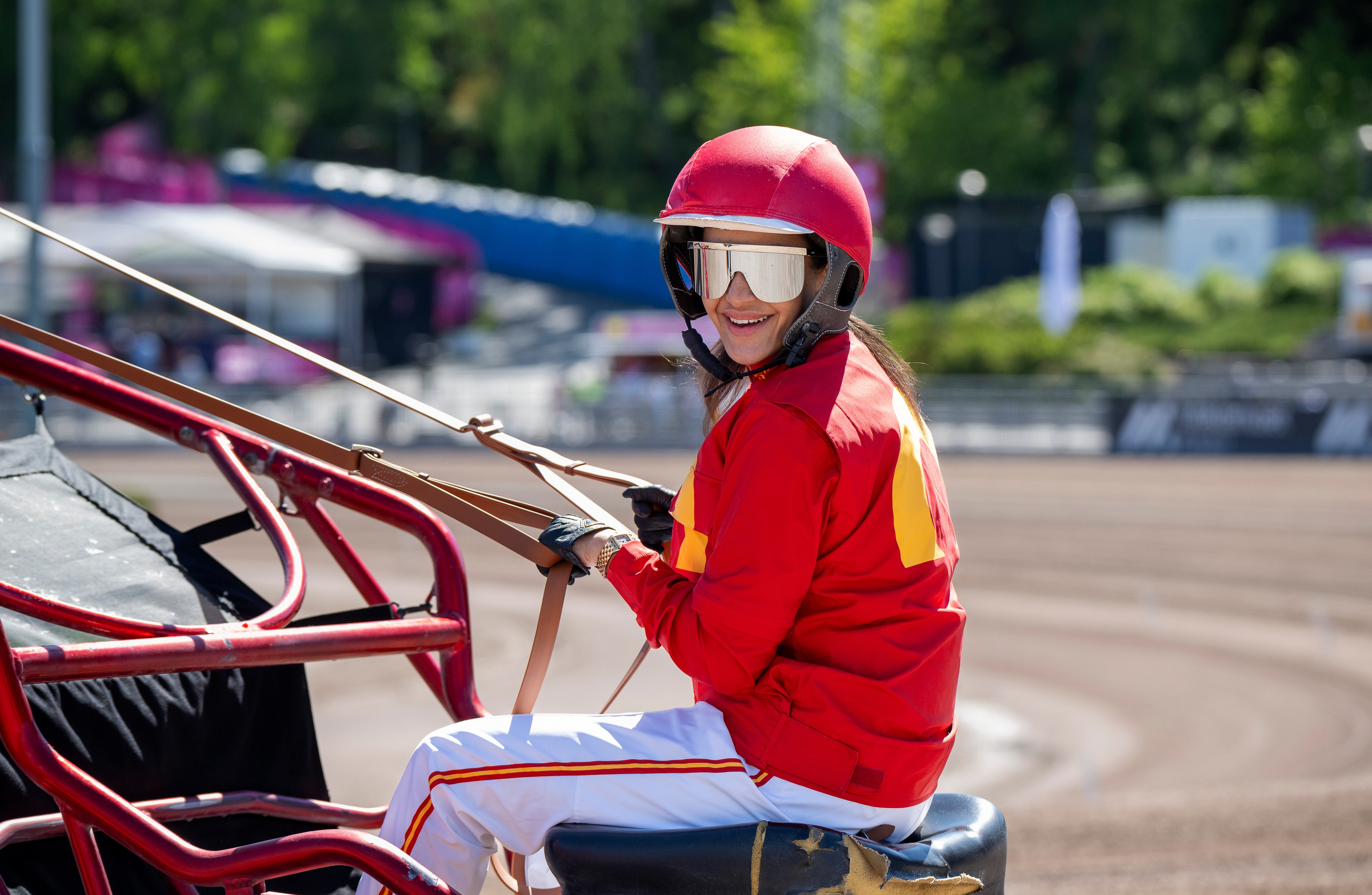 Person i röd hjälm och röd jacka sitter på en travhäst vid Solvalla travbana.