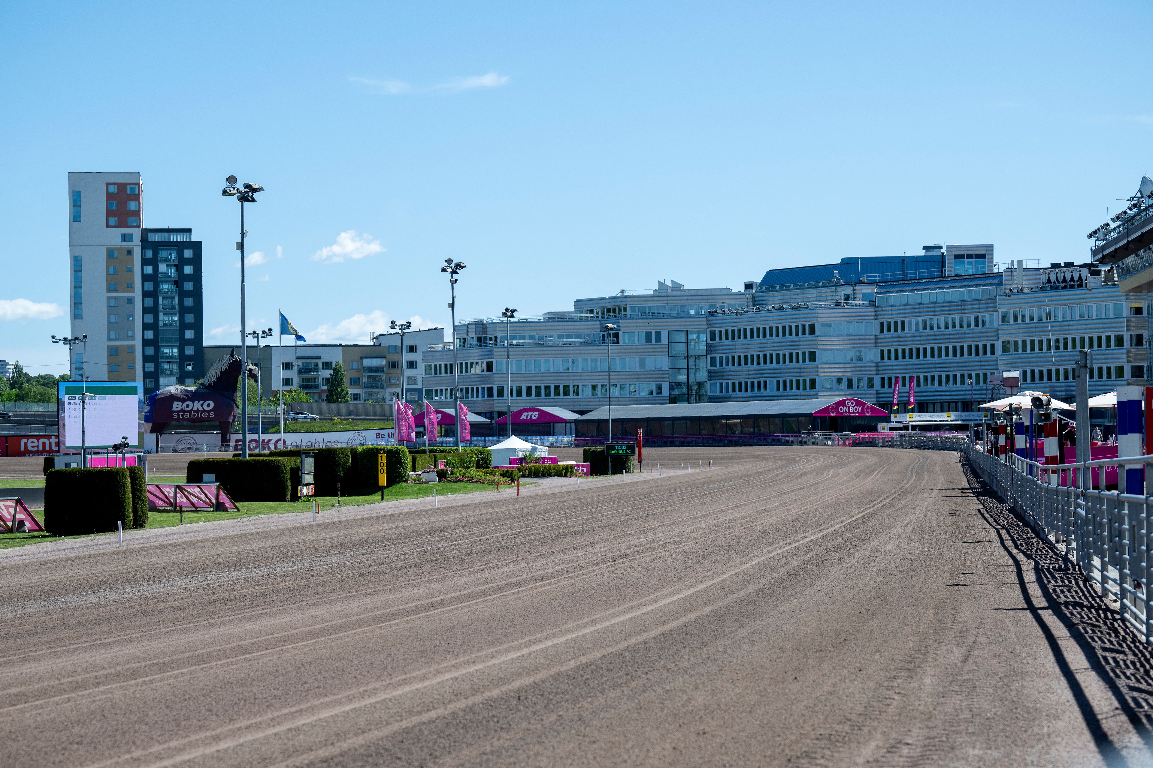 Solvalla travbana med en tom löparbana i förgrunden. I bakgrunden syns moderna byggnader, tävlingsfaciliteter och publikläktare under en klar sommarhimmel.