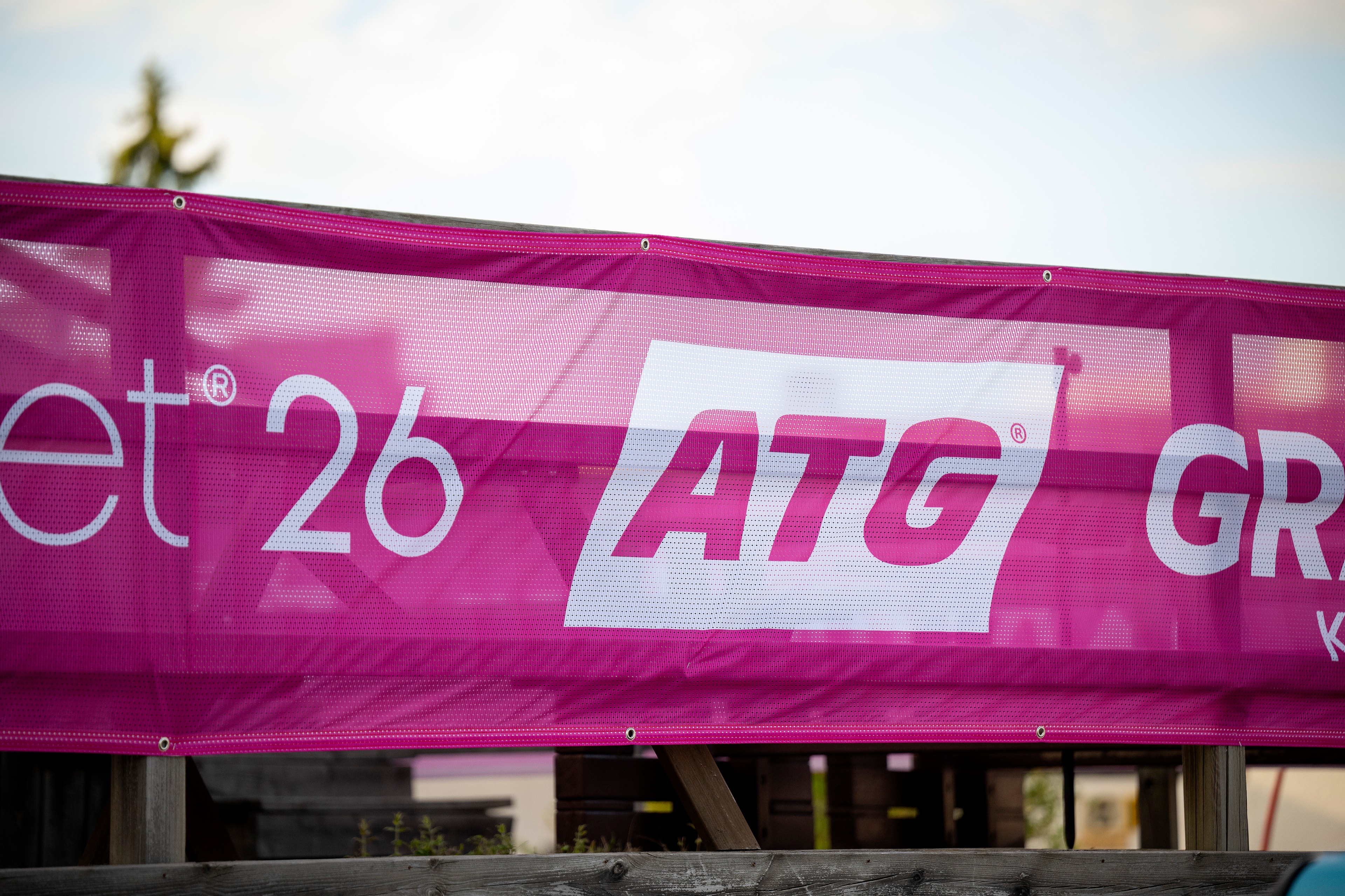 Rosa skylt med ATG-logotyp och text på en byggnad, fotograferad mot en ljus himmel.
