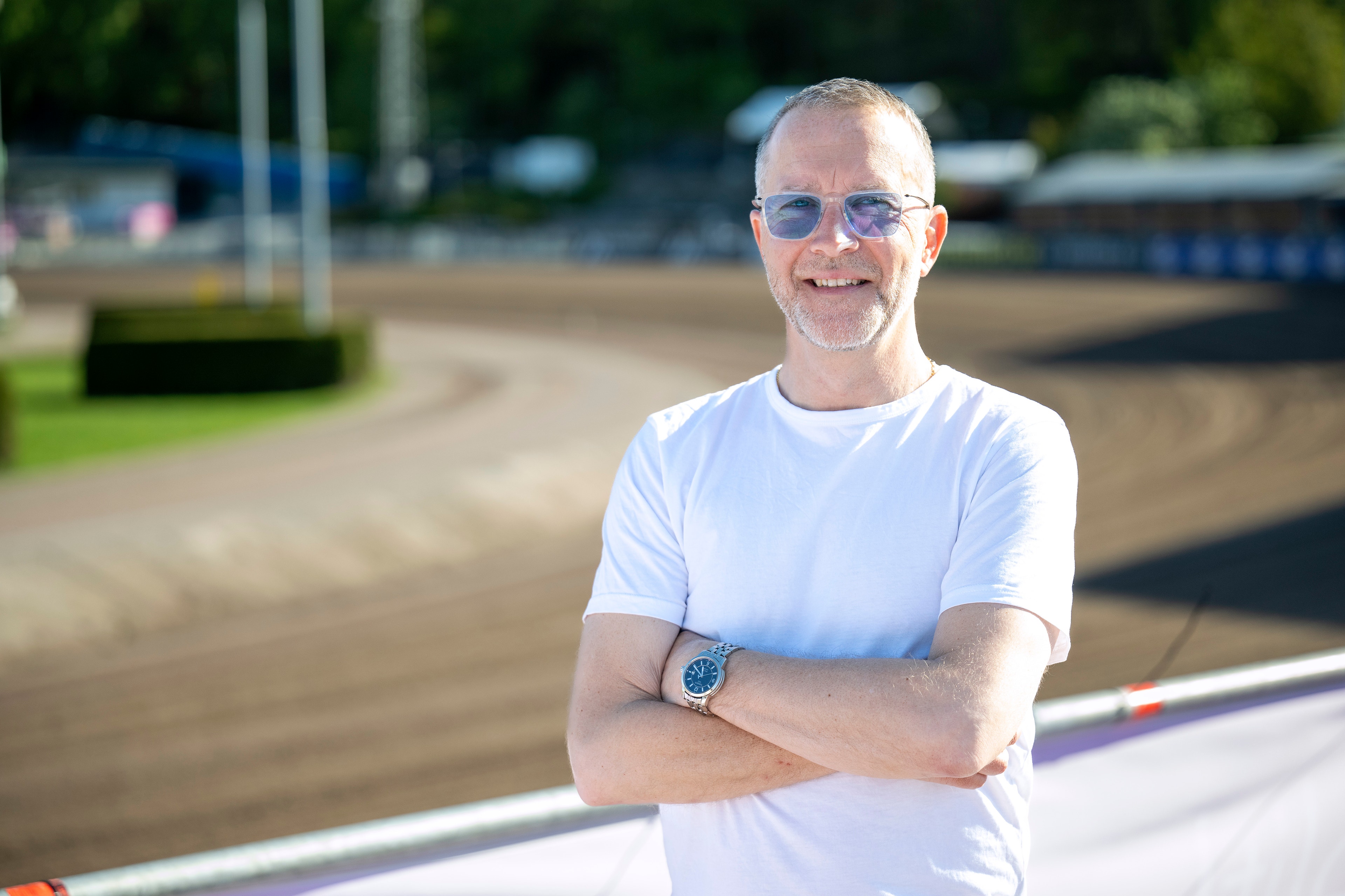 Porträtt av en man med glasögon i vit t-shirt som står utomhus vid en sportanläggning.