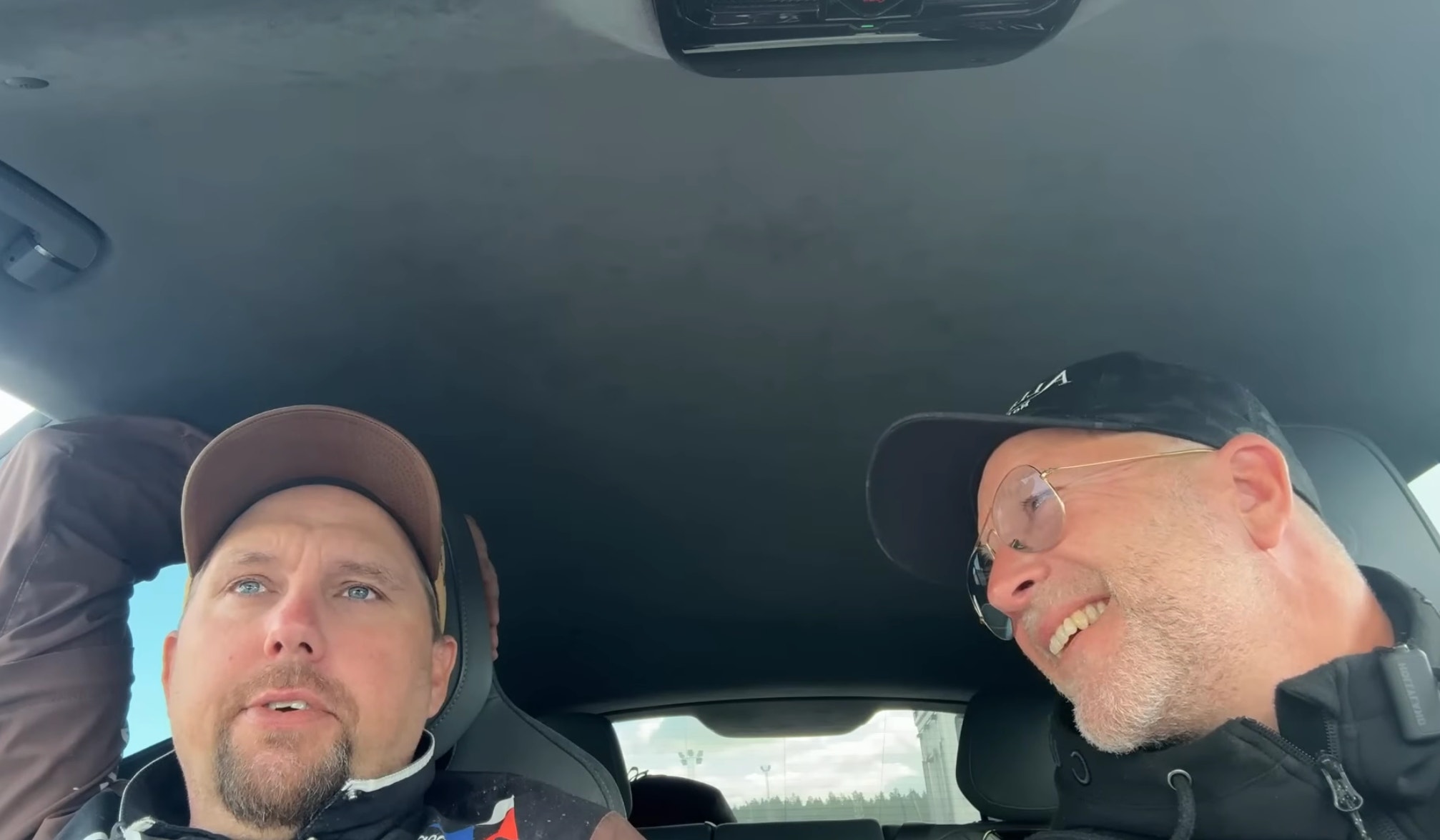 Två män i en bil tar en selfie tillsammans. Båda ler mot kameran.