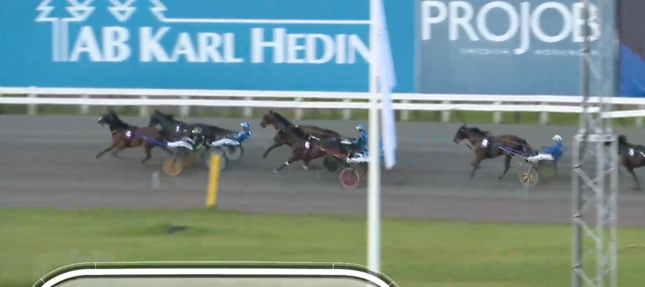 Hästar med sulkyer under ett travlopp på en travbana. Flera hästar är i full galopp under tävlingen.