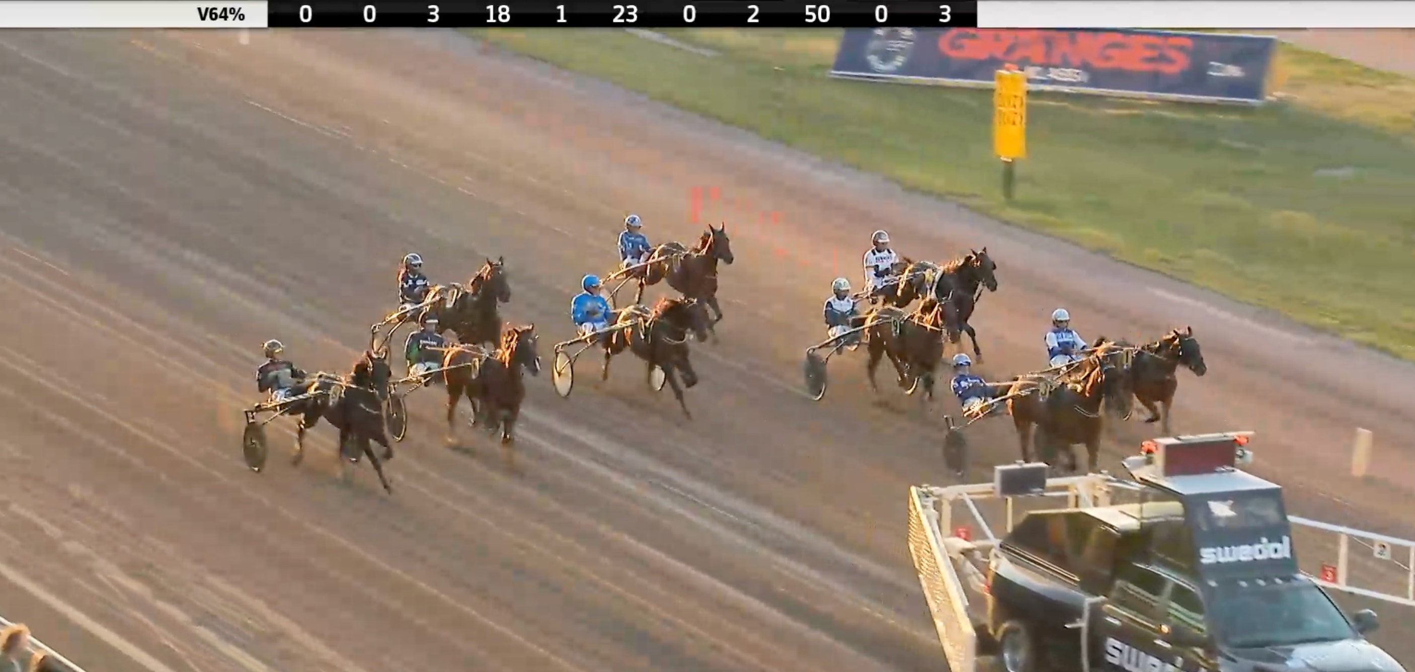 Flera hästar med kuskar tävlar på en sandtrack under ett hästkapplöpningslopp.