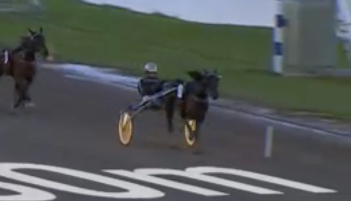 En häst med kuskar i en sulky under ett travlopp på en racingbana.
