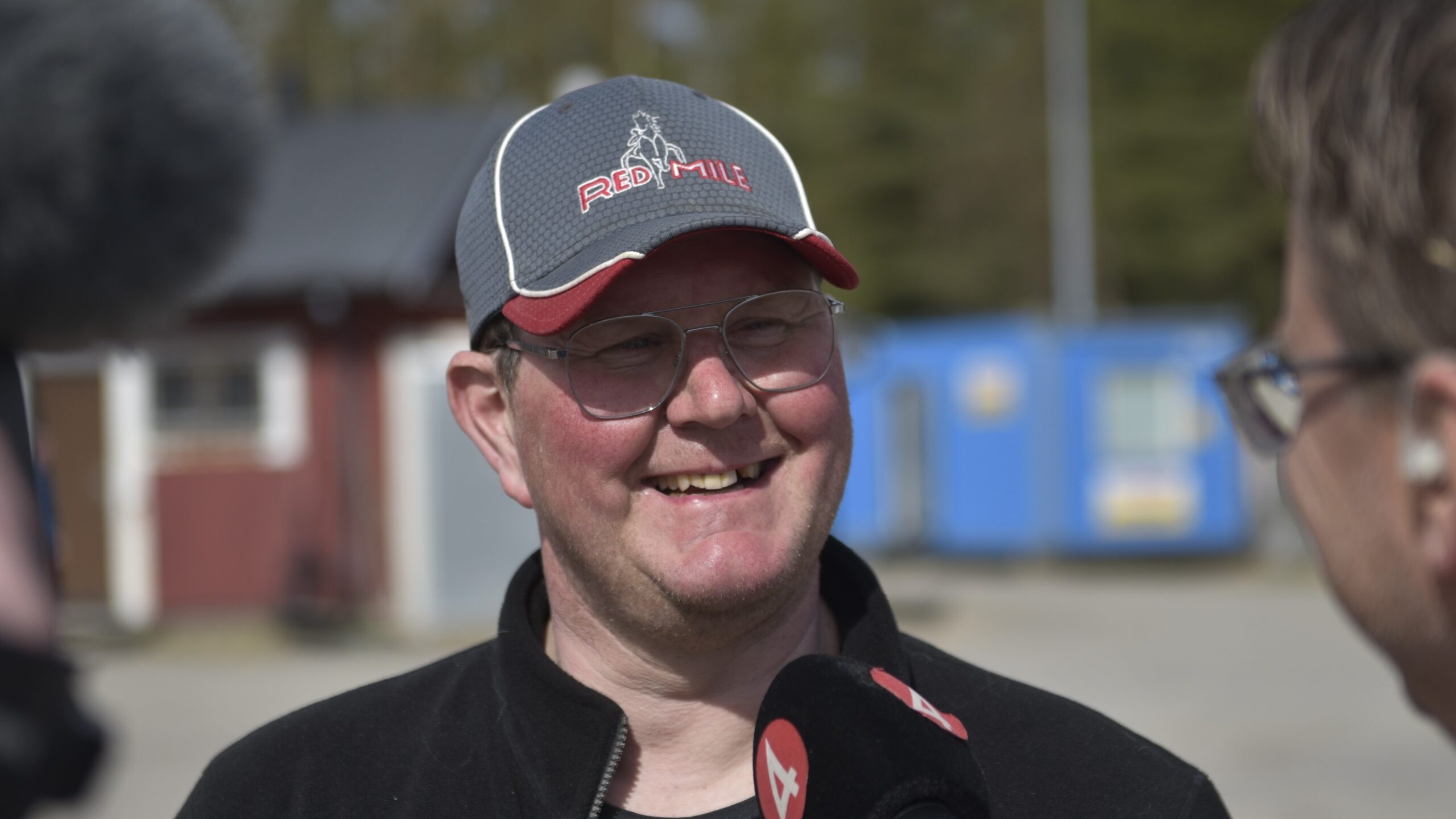 En leende man i keps intervjuas utomhus med en mikrofon.