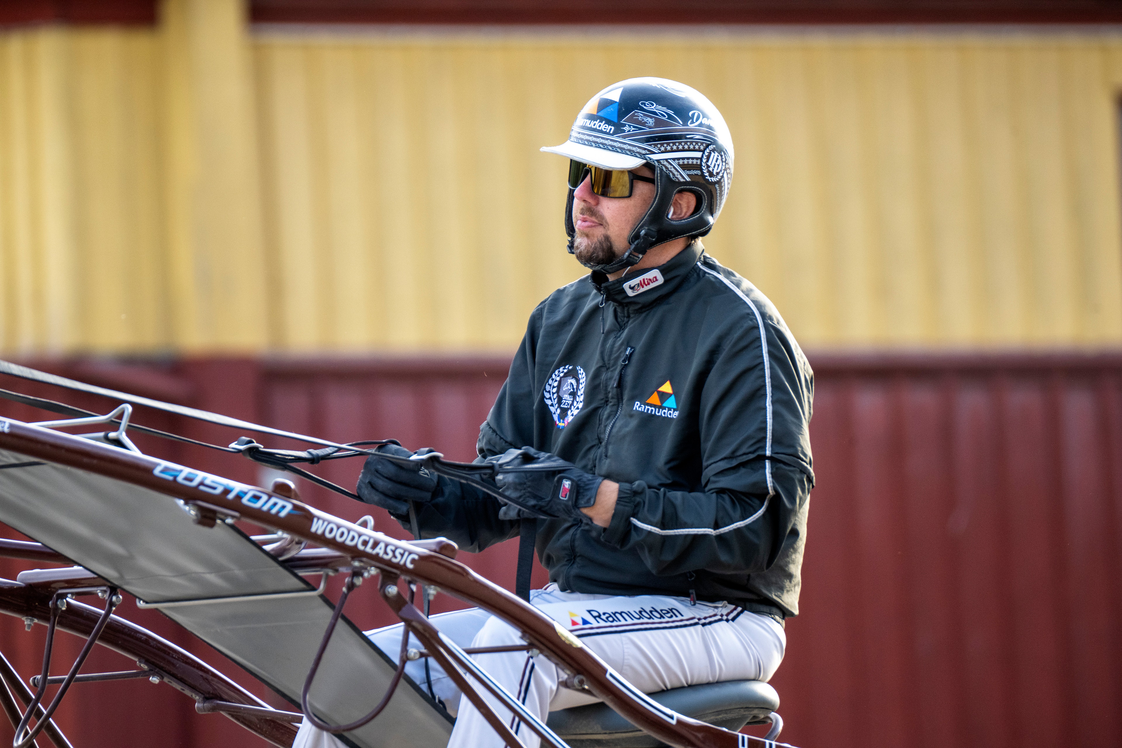 En cyklist i blå hjälm och svart jacka sitter på en cykel framför en gul och röd vägg.