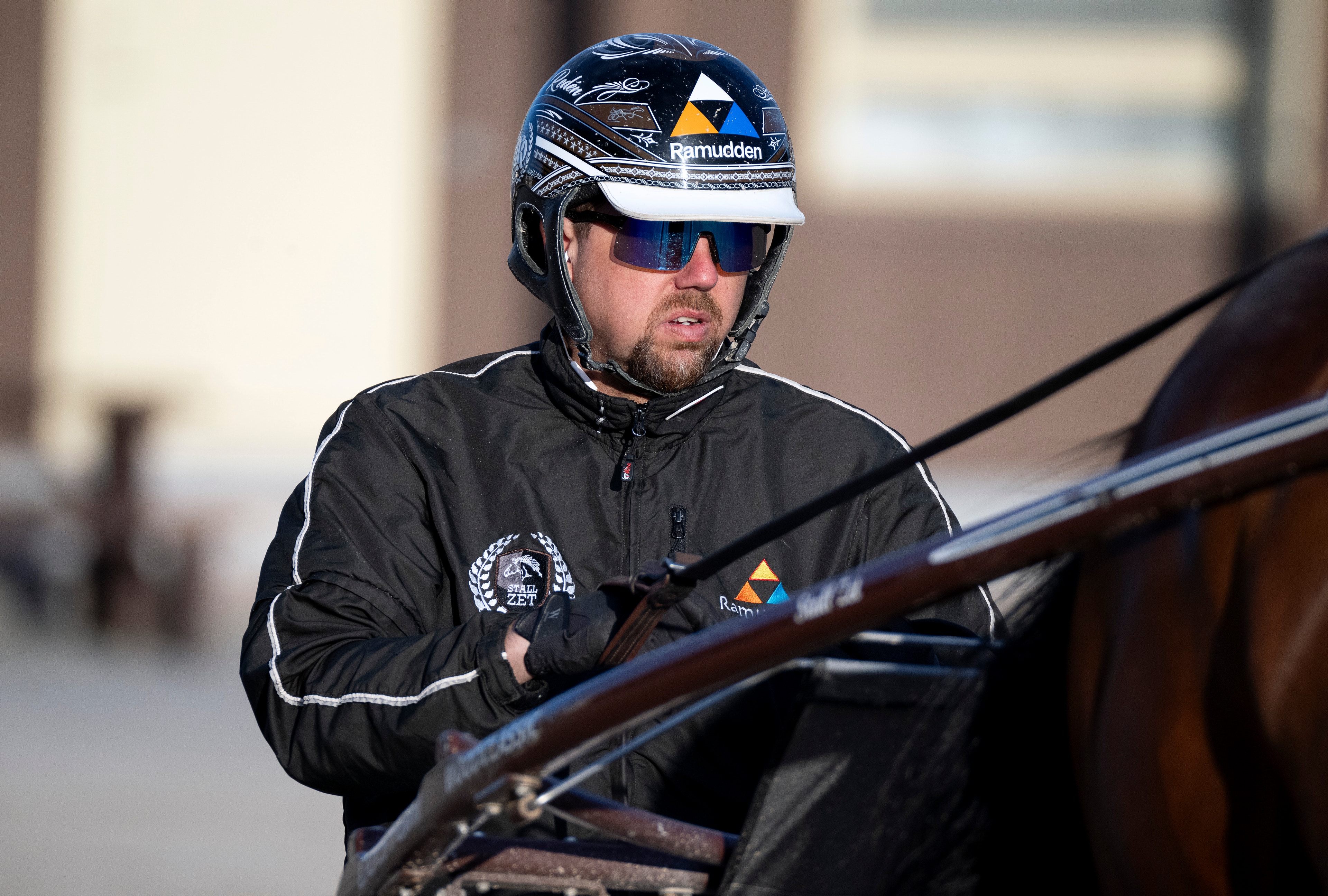 En man i svart jacka och cykelhjälm håller i tyglar till en häst. Daniel Rede